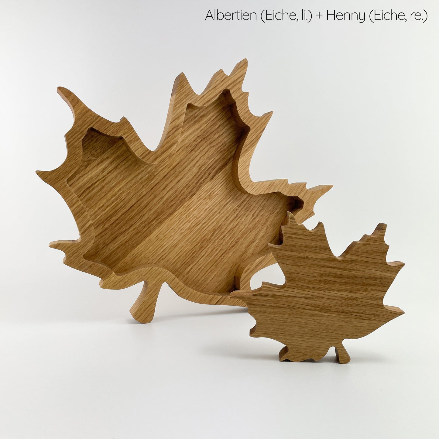 Eine Blatt aus Holz in Form eines Ahornblattes und ein kleineres Blatt aus Holz zur Dekoration vor weißem Hintergrund. Beide Blätter sind schräg mit dem Stiel nach unten aufgestellt und zeigen deutlich die Maserung des Eichenholzes.