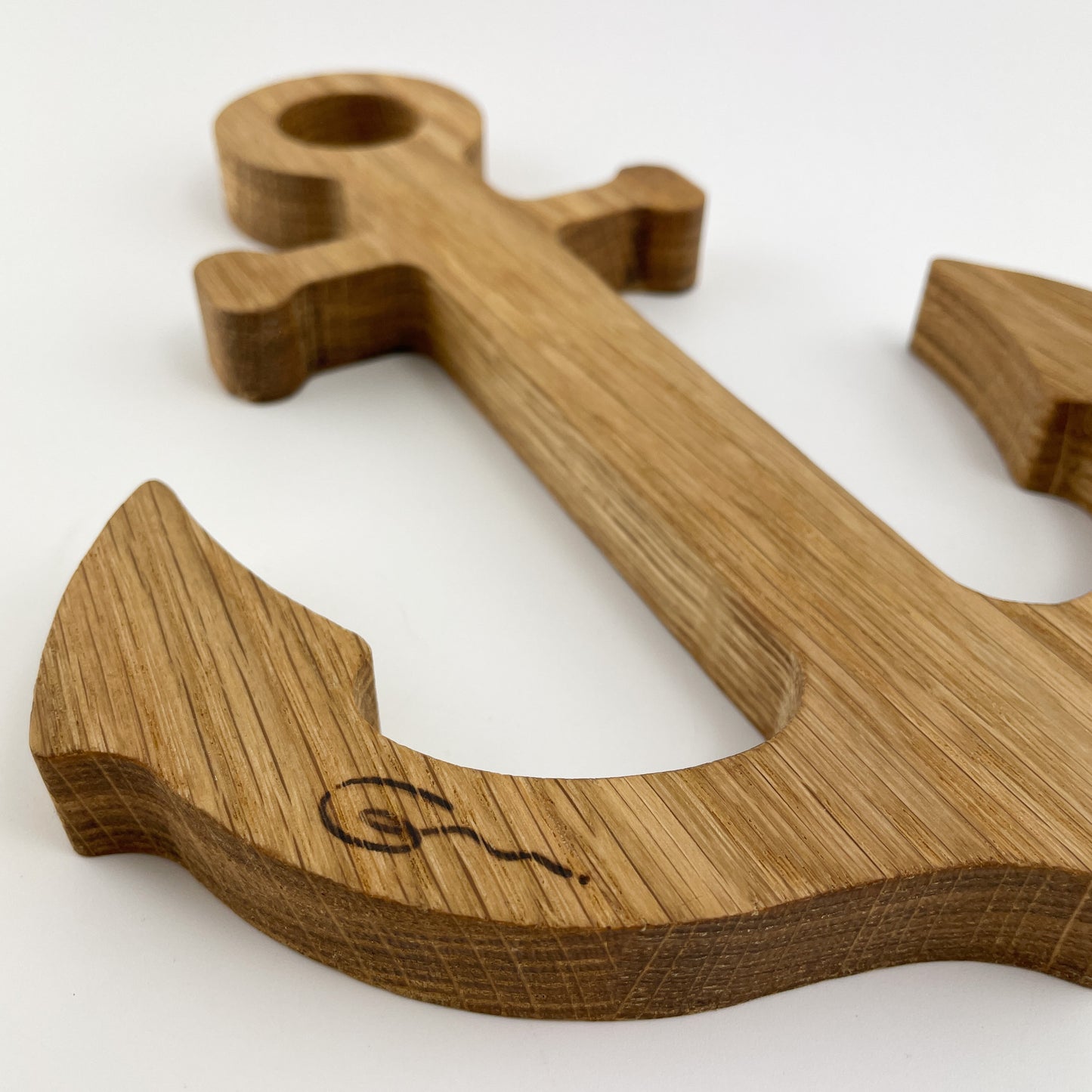 Detailansicht von der Dekoanker aus Holz - Pelle, mit dem eingebrannten Logo der Goertz Möbelmanufaktur. Das Logo zeichnet sich dunkelbraun vom Rest des Holzes ab und die Maserung ist gut erkenntbar.