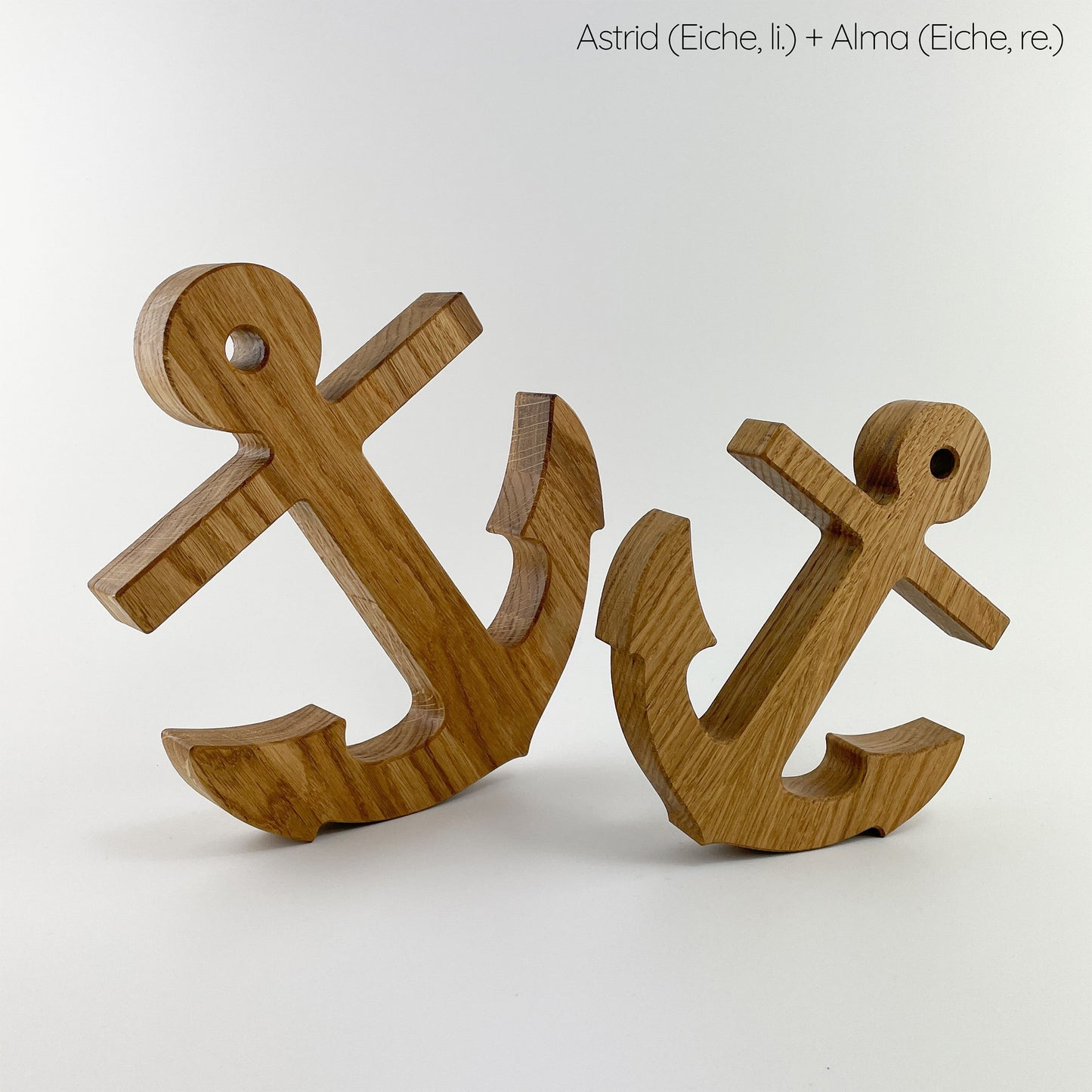 Ein größerer Dekoanker aus (Eichen-)Holz links und rechts daneben ein kleinerer ebenfalls aus Eiche. Beide Anker sind vor einem weißen Hintergrund fotografiert, stehen schräg und zeigen mit den Köpfen voneinander weg.