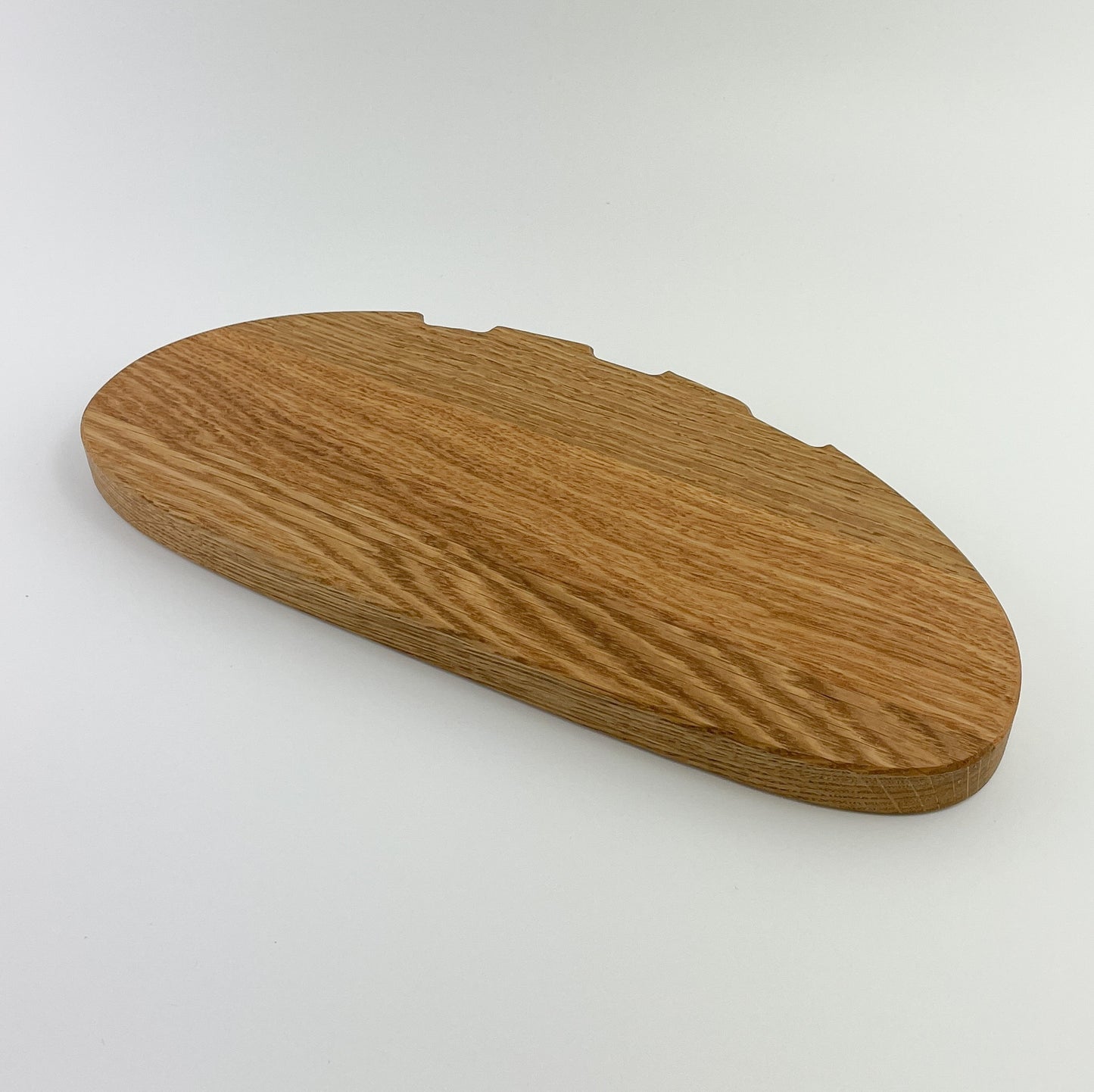 Frontansicht von Holz Schneidebrett - Bernd. Ein ovales Schneidebrett aus Holz mit deutlich sichtbarer Maserung und abgerundeten Kanten auf einem einfarbigen hellen Hintergrund. Die Textur des Holzes zeigt verschiedene Brauntöne, die eine natürliche und rustikale Ästhetik vermitteln.