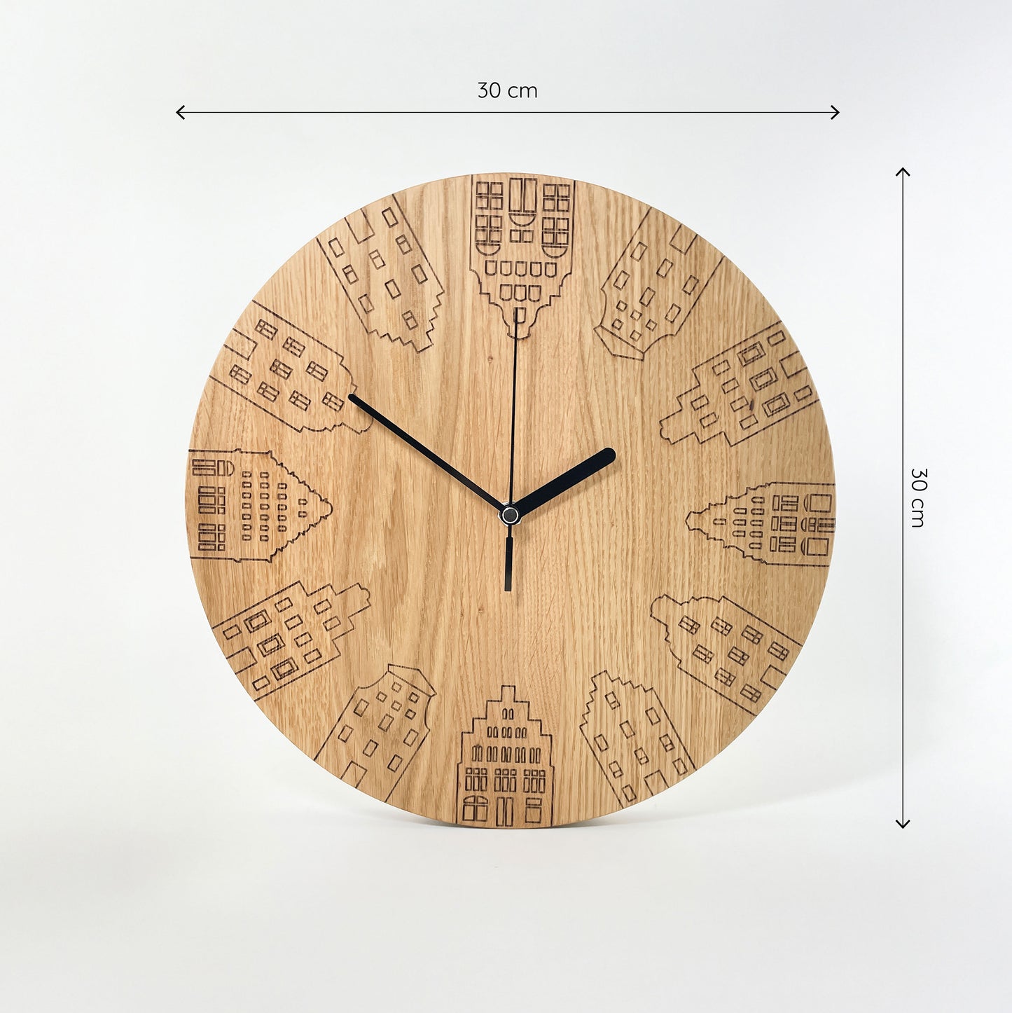 Frontalansicht einer Runden Wanduhr aus Massivem Eichenholz (Maserung verläuft vertikal/ aufrecht) mit schwarzen Zeigern vor weißem Hintergrund. Das Zifferblatt ist gelasert und zeigt 12 verschiedene Giebelhäuser, die Umlaufend am Rand der Uhr sitzen an Stelle der Zahlen. Oberhalb und rechts von der Uhr befinden sich zwei Maßketten, welche ihre Größe angeben - sie ist im Durchmesser 30cm breit.