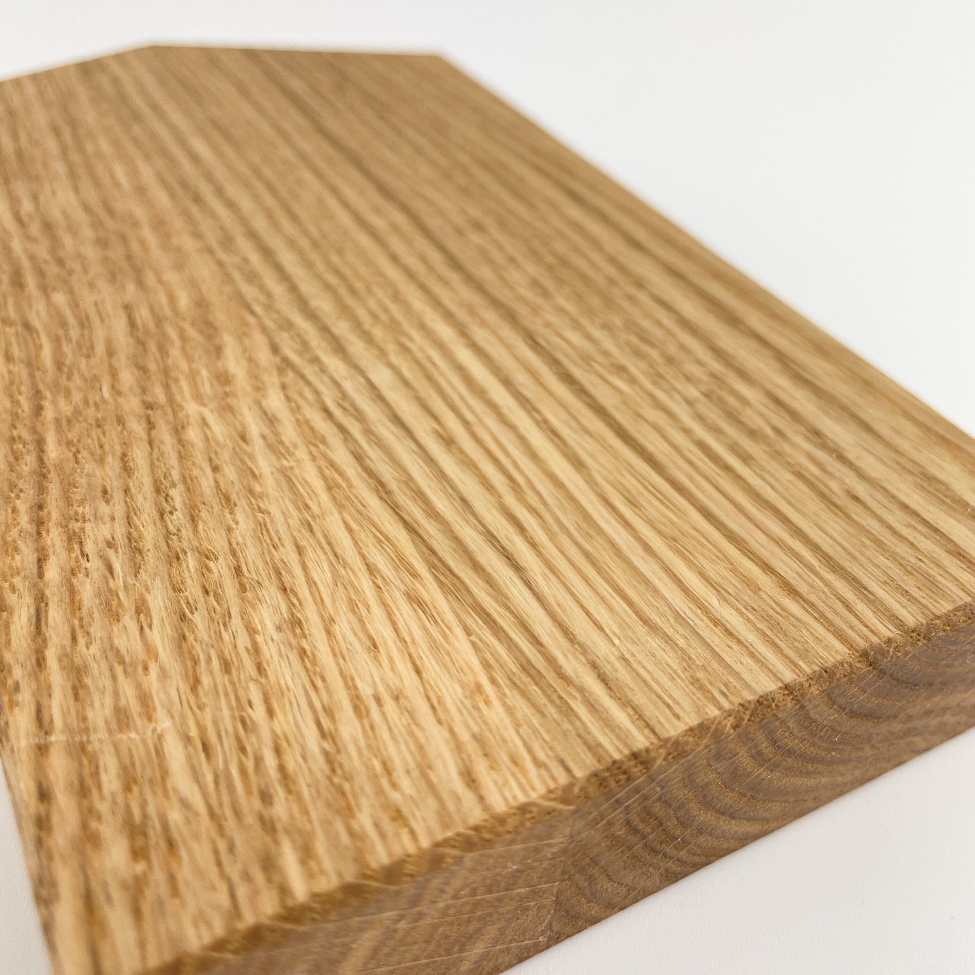 Detailaufnahme des Deko-Hauses aus massivem Eichenholz vor weißem Hintergrund. Zu sehen ist der untere Bereich des Hauses und die gefaste Kante sowie die Maserung des Holzes.