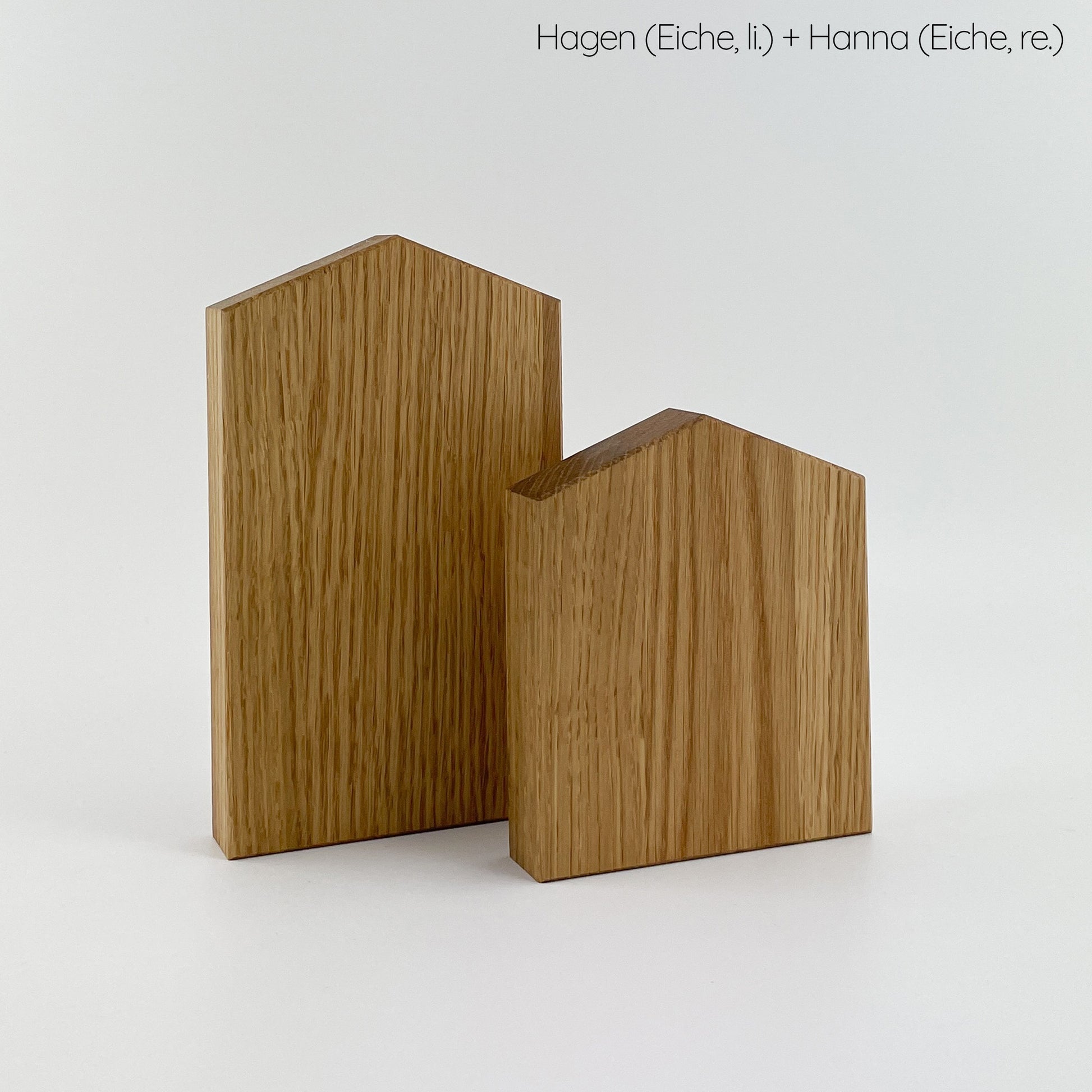 Zwei minimalistische Holz Dekohaus, namens Hagen und Hanna, aus Eichenholz gefertigt. Hagen steht links, während Hanna rechts steht. Die glatte Oberfläche zeigt sichtbare Holzmaserungen und schafft eine warme und organische Ästhetik.