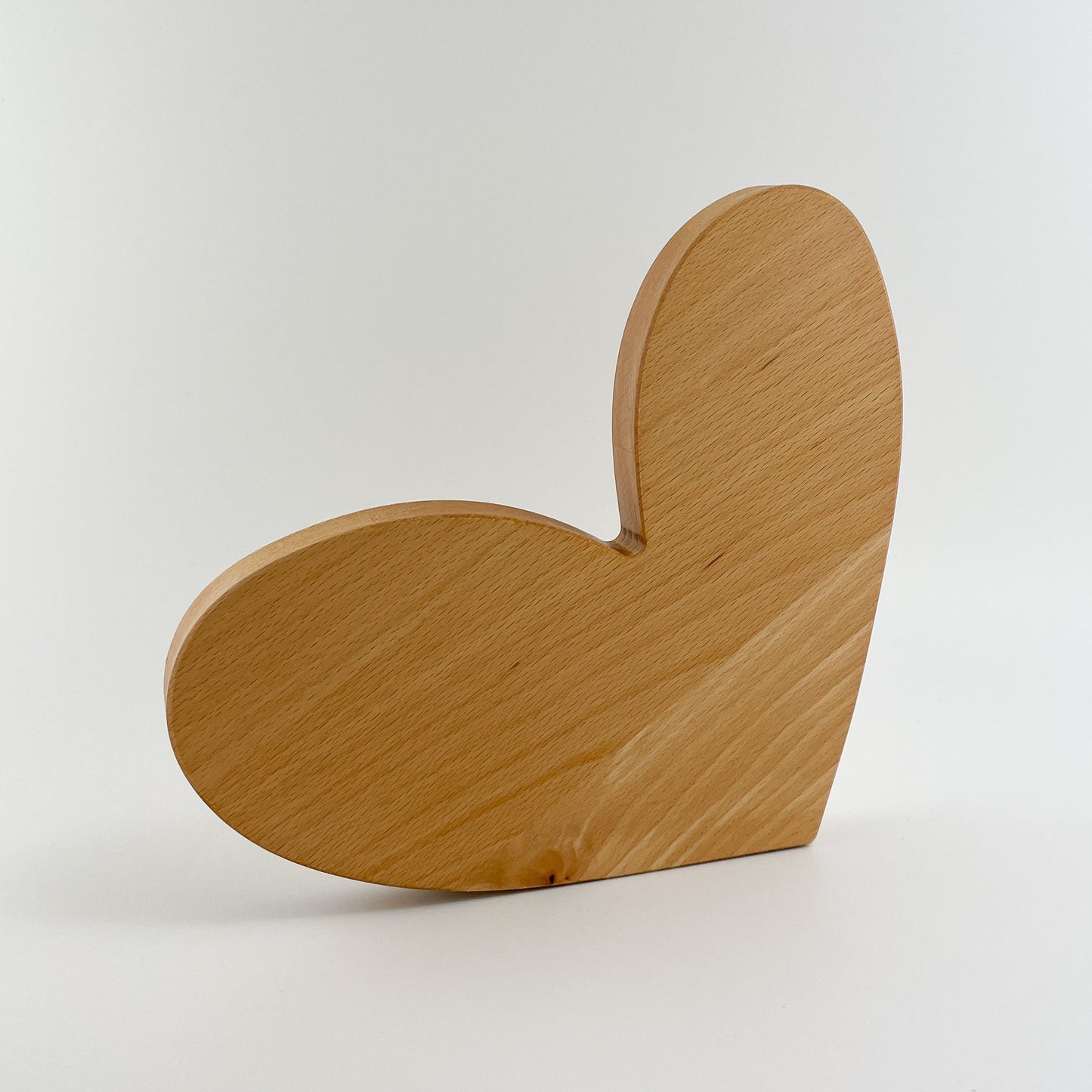 Rückansicht ein handgefertigtes Holzherz steht im Zentrum des Bildes. Die Maserung des Holzes ist deutlich sichtbar und verleiht dem Herz eine natürliche und einzigartige Textur. Das Licht fällt sanft auf das Holz, wodurch die warmen Brauntöne hervorgehoben werden und das Herz dreidimensional wirkt.