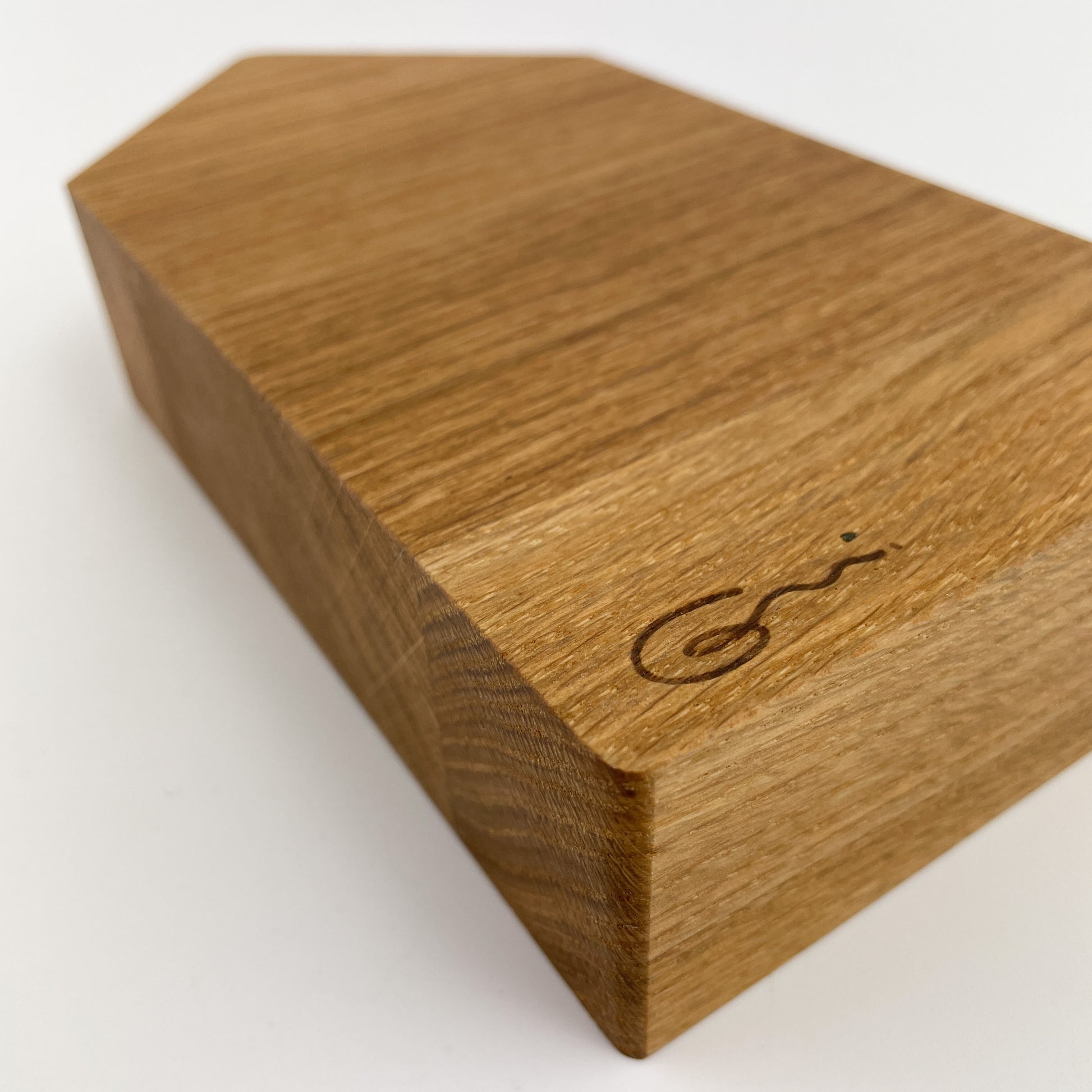 Detailansicht von Holz Dekohaus mit glatter Oberfläche und sichtbarer Holzmaserung. Auf einer der schmaleren Seiten befindet sich eine kleine, dunkle Gravur oder Markierung, die eine gebogene Signatur darstellt.