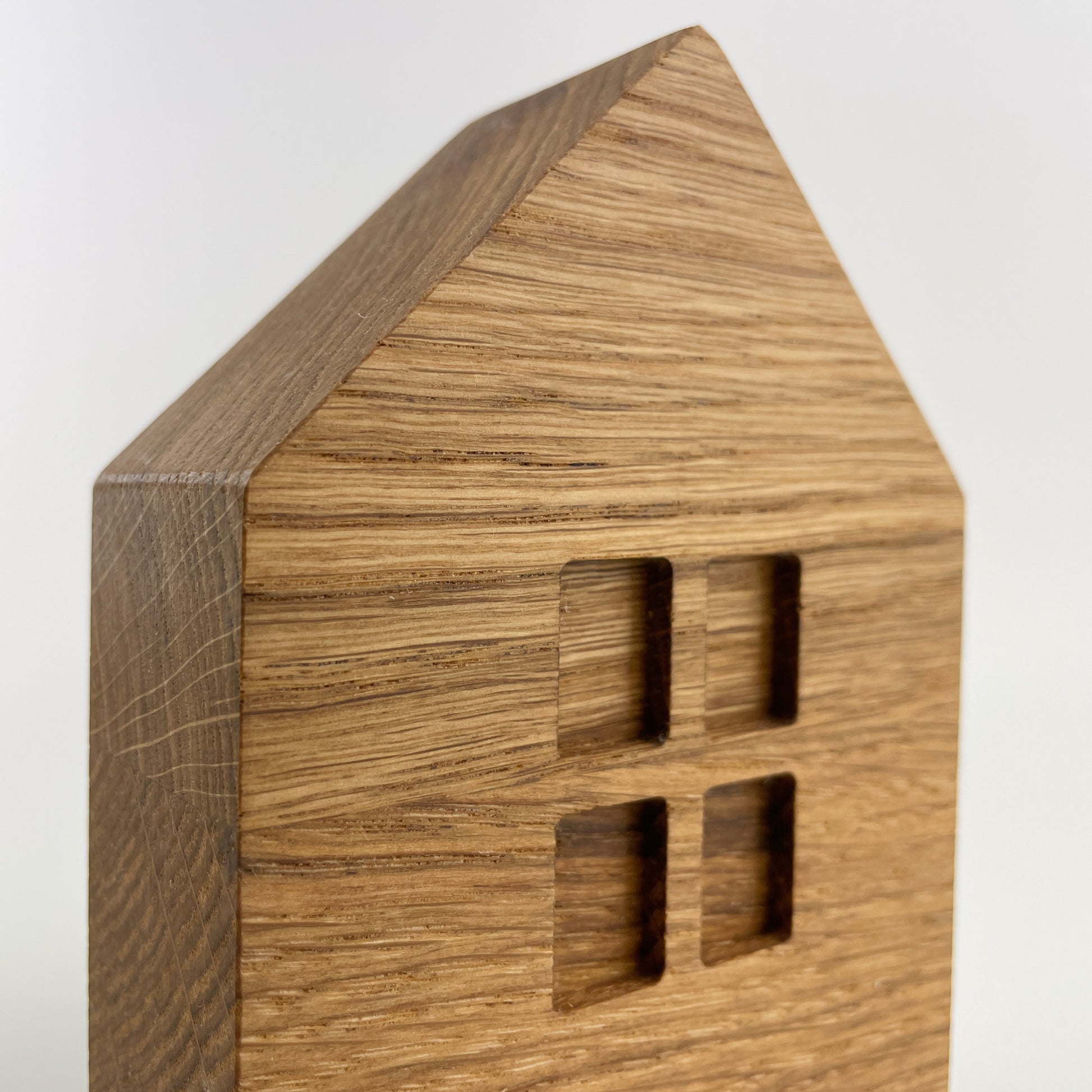 Detailansicht von Holz Dekohaus in Form eines vereinfachten Hauses mit spitzem Dach. Das Holz hat eine markante Maserung und ist glatt. Es gibt vier rechteckige Ausschnitte.