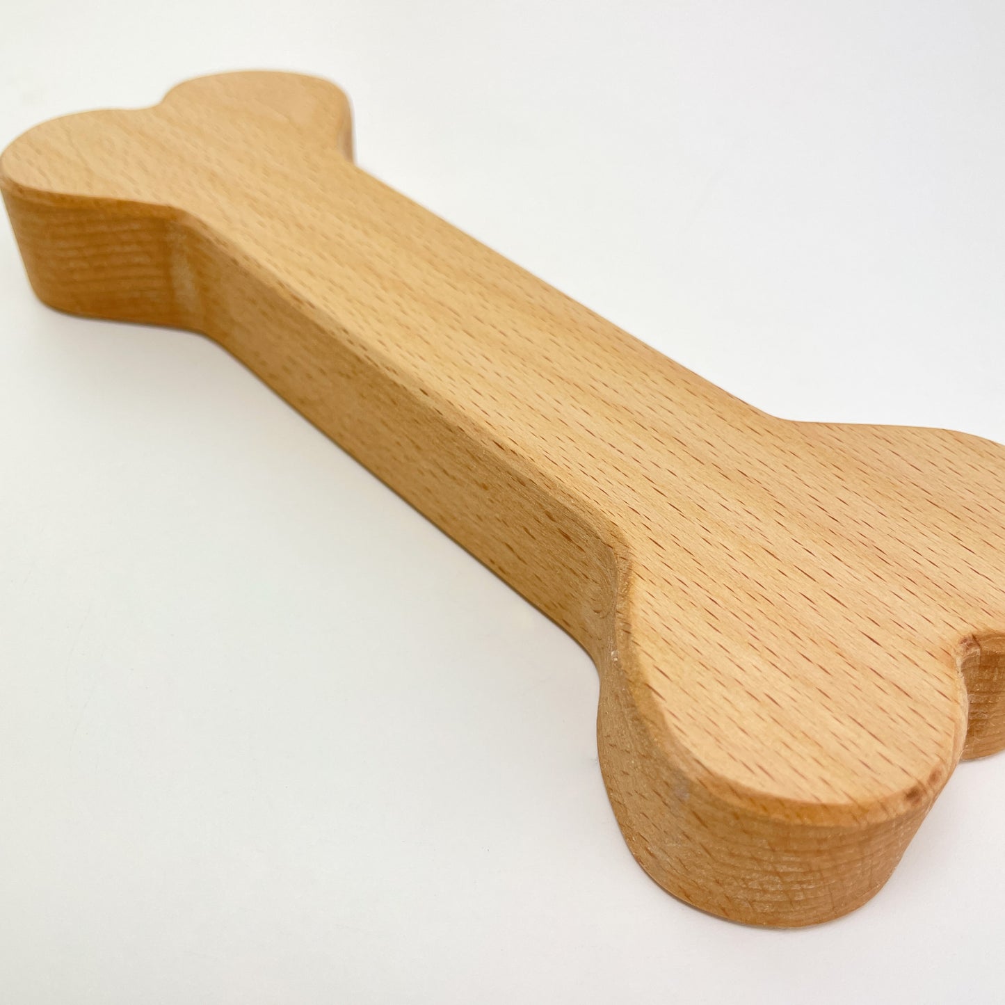 Detailaufnahme eines Holz-Knochens zur Dekoration vor weißem Hintergrund. Der Fokus liegt auf einem Ende des Knochens und er ist schräg von unten rechts nach oben links im Bild angeordnet. Die Kante des Deko-Knochens ist gefast.