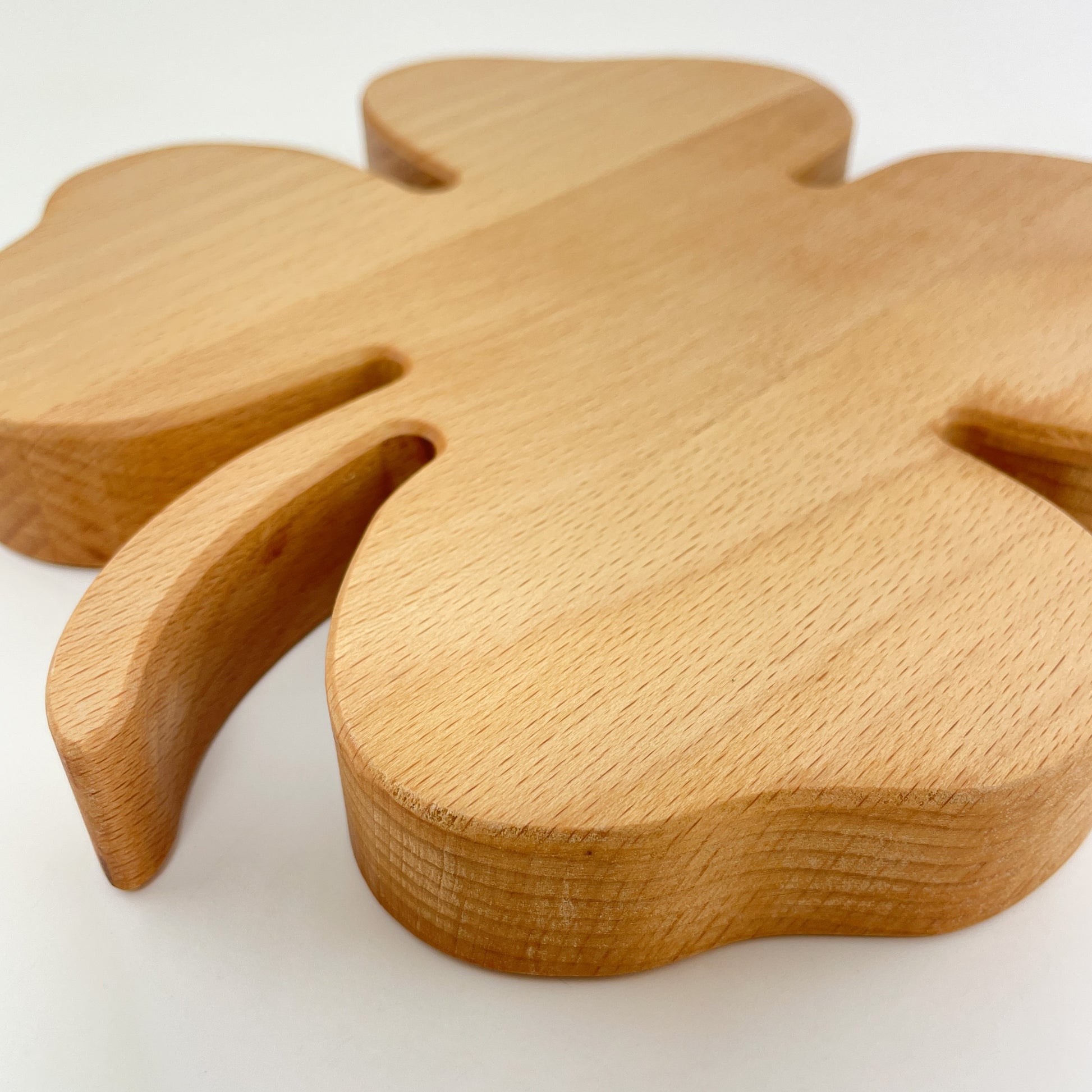 Detailaufnahme des Deko-Kleeblattes aus Buchenholz vor weißem Hintergrund. Im Fokus steht der Stiel des Blattes und die Kantenverarbeitung sowie die Holzmaserung sind gut zu erkennen.