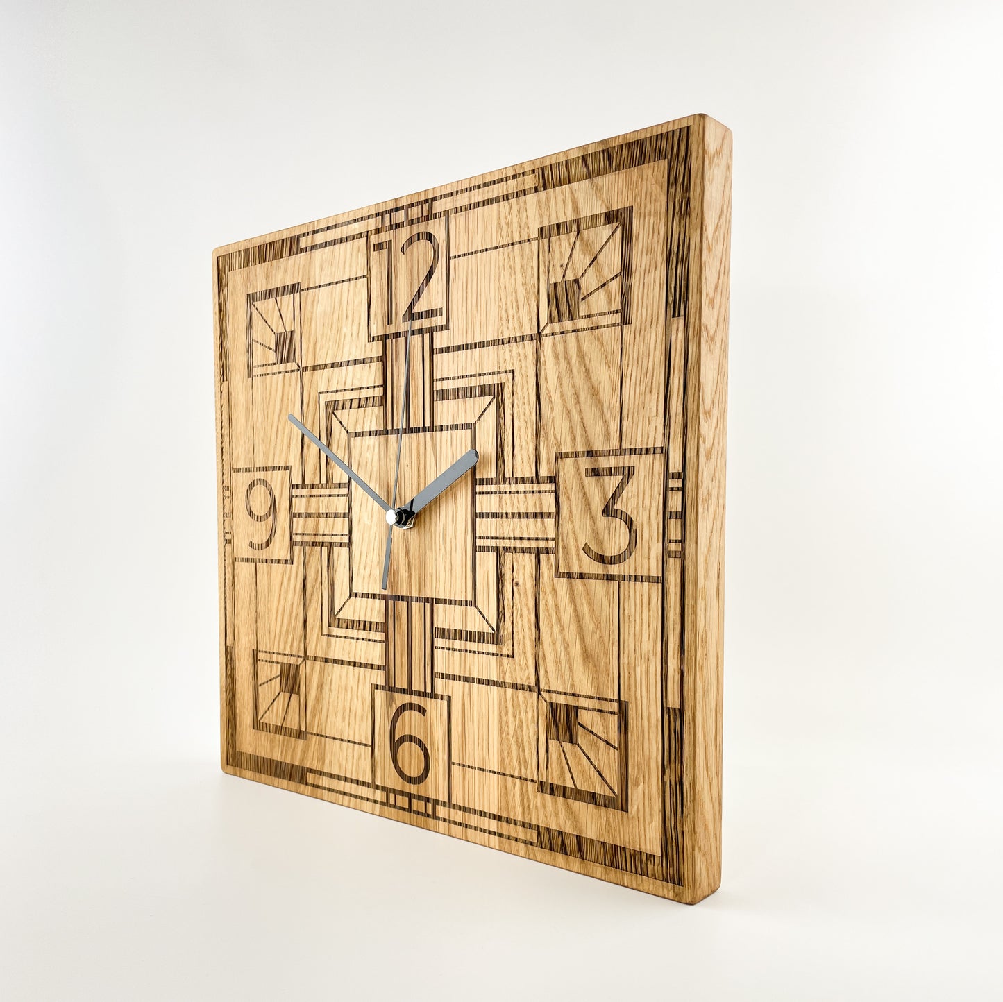 Ansicht einer eckigen Wanduhr aus Massivem Eichenholz (Maserung verläuft vertikal/ aufrecht) mit schwarzen Zeigern vor weißem Hintergrund. Das Zifferblatt ist gelasert und zeigt ein modernes geometrisches Art-Decó-Muster, mit markanten Linien sowie den Zahlen 12, 3, 6 und 9 als stilisierte Stundenmakierung.