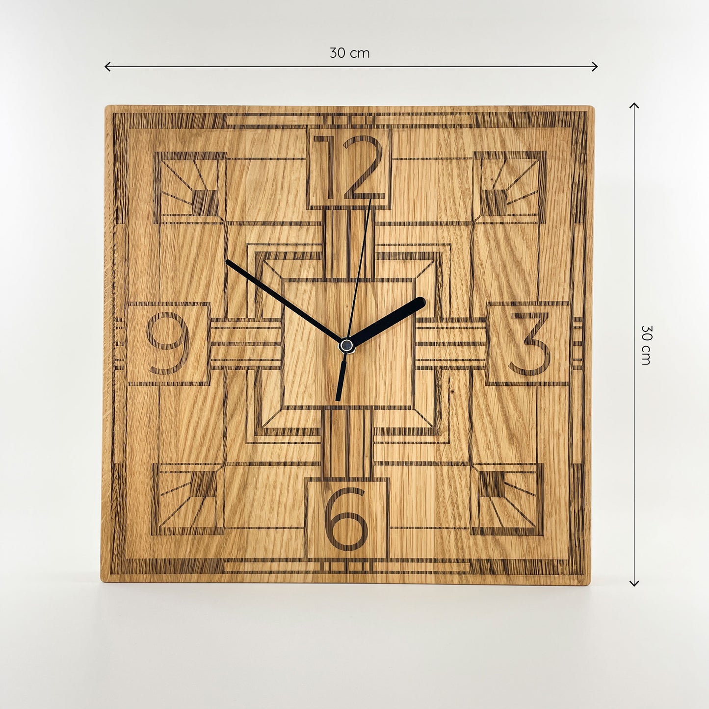 Frontalansicht einer eckigen Wanduhr aus Massivem Eichenholz (Maserung verläuft vertikal/ aufrecht) mit schwarzen Zeigern vor weißem Hintergrund. Das Zifferblatt ist gelasert und zeigt ein modernes geometrisches Art-Decó-Muster, mit markanten Linien sowie den Zahlen 12, 3, 6 und 9 als stilisierte Stundenmakierung. Oberhalb und rechts von der Uhr befinden sich zwei Maßketten, welche ihre Größe angeben - Länge und Höhe sind mit 30cm angegeben.
