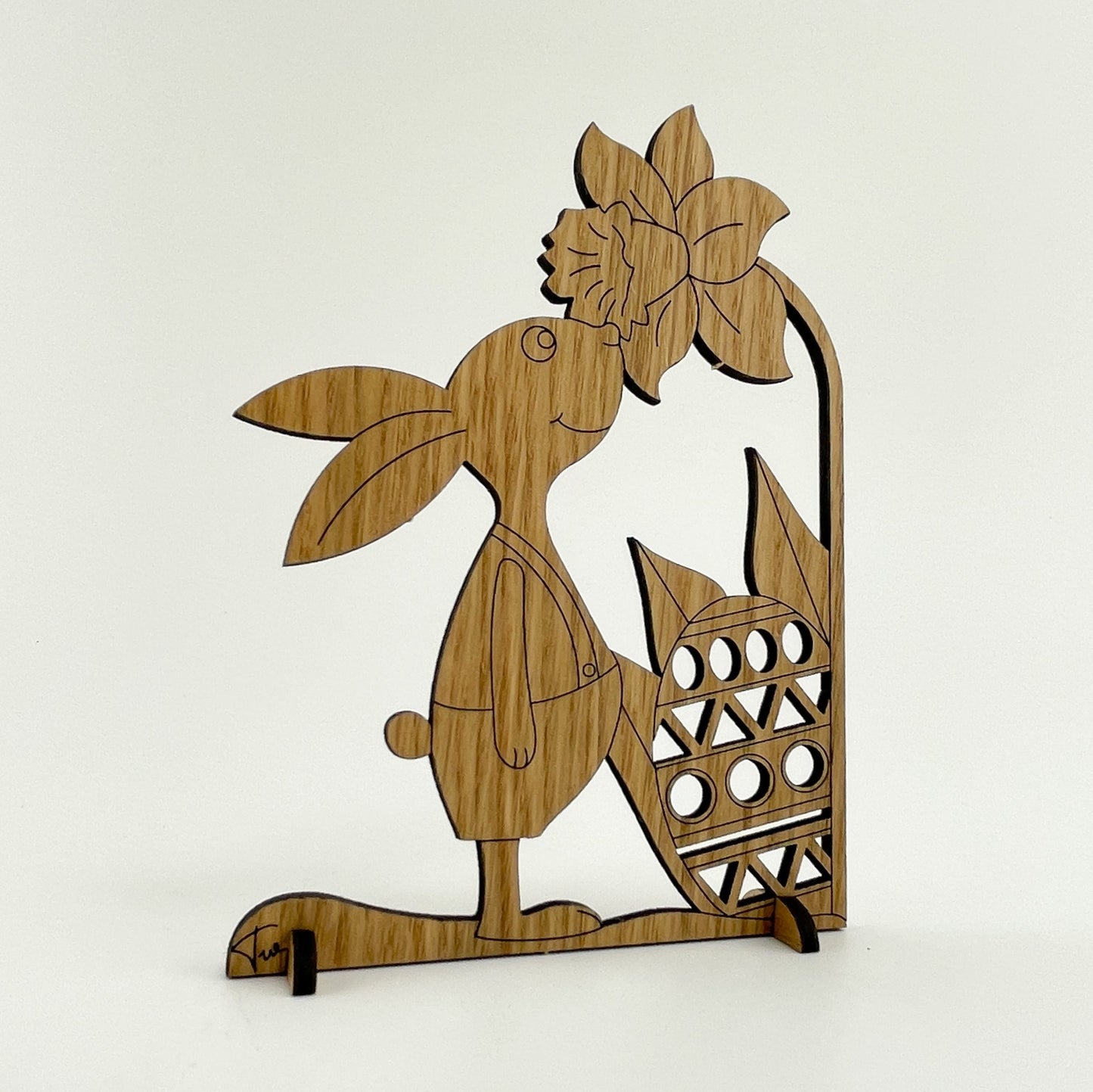 Rückseite von Holz-Osterkarte Pino ist eine künstlerisch gestaltete Osterkarte aus Holz mit einer stehenden Hasenfigur. Diese Figur besteht aus mehreren Holzschichten, die sorgfältig übereinander gelegt wurden, um einen dreidimensionalen Effekt zu erzielen. Die Details der Figur sind beeindruckend: Die Körperform und die Gesichtszüge des Hasen werden durch feine Linien und Konturen hervorgehoben.