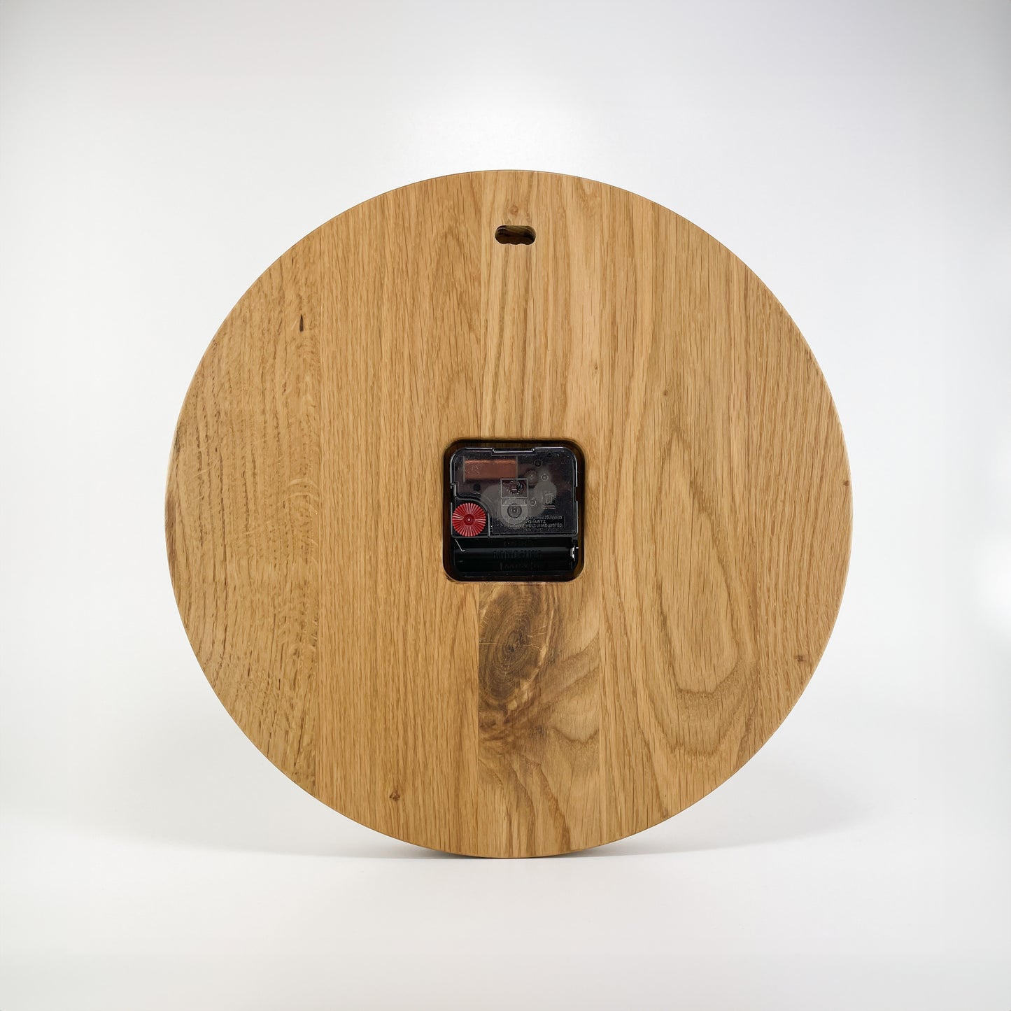 Rückansicht einer runden Holz-Wanduhr. Wandaufhängung im oberen Bereich sowie sichtbares Batteriefach und Einstellungsrad für die Zeiger.