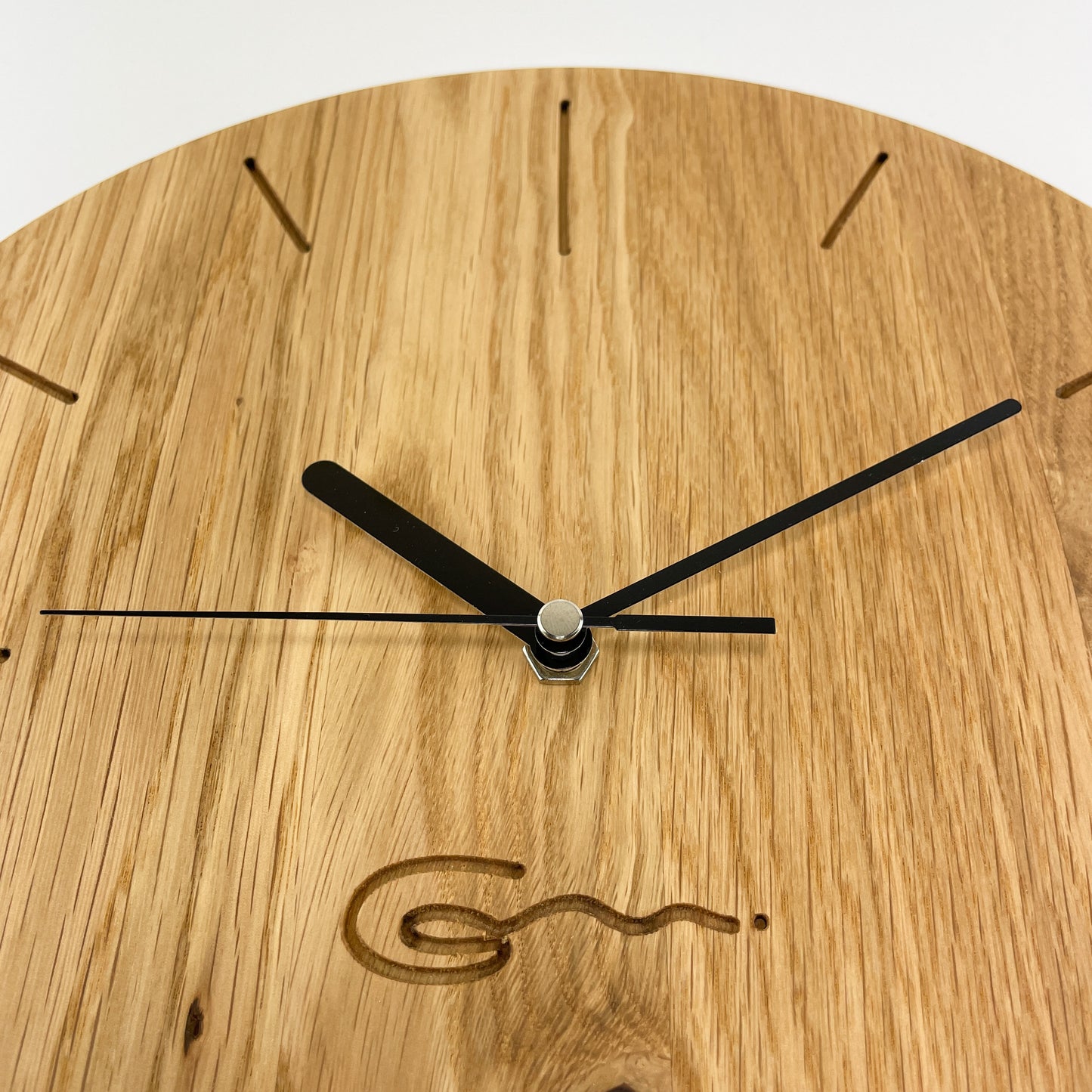 Detailansicht einer runden Holz-Wanduhr mit schwarzen Zeigern, bei der die Stunden durch Striche gekennzeichnet sind.