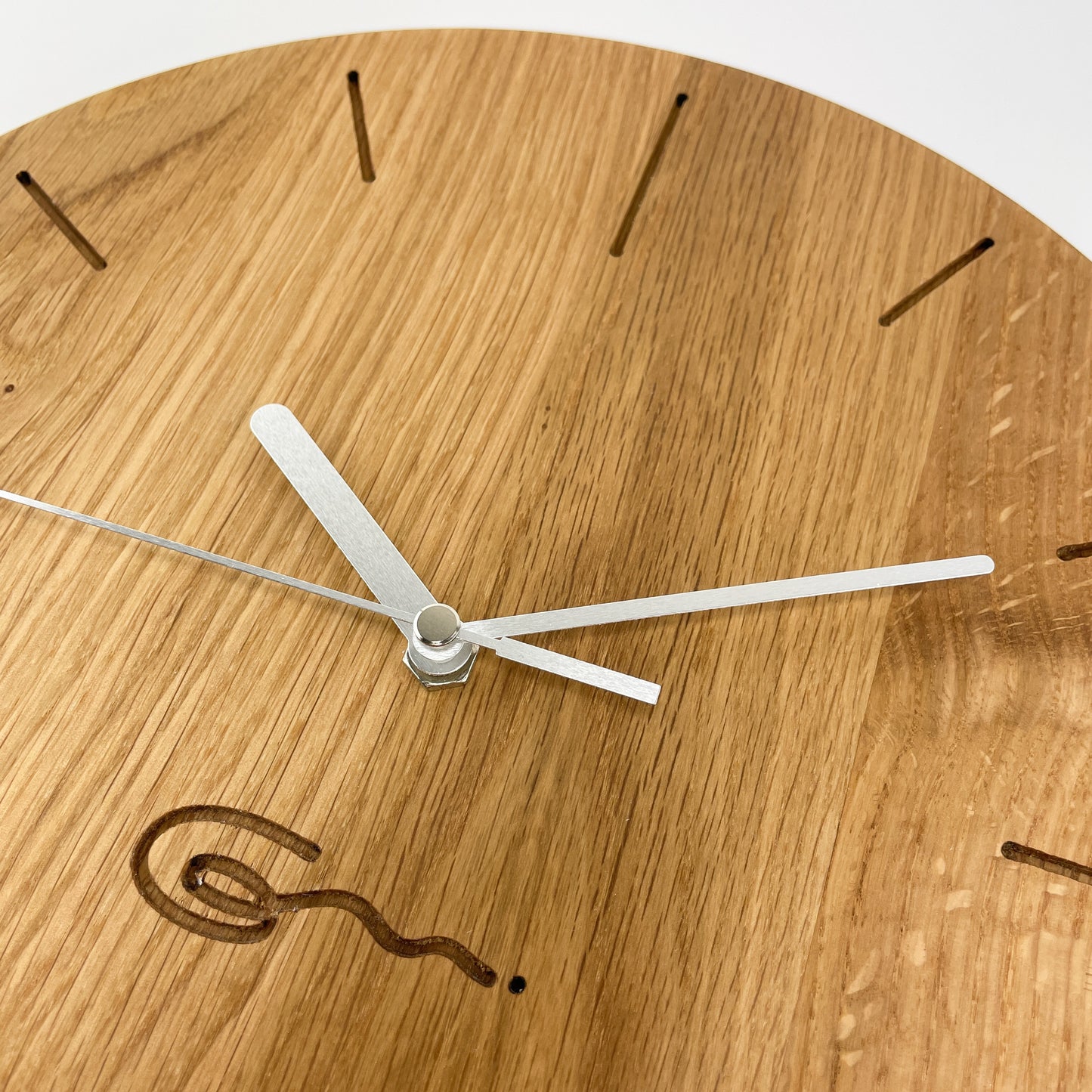 Detailansicht einer runden Holz-Wanduhr mit silbernen Zeigern, bei der die Stunden durch Striche gekennzeichnet sind.