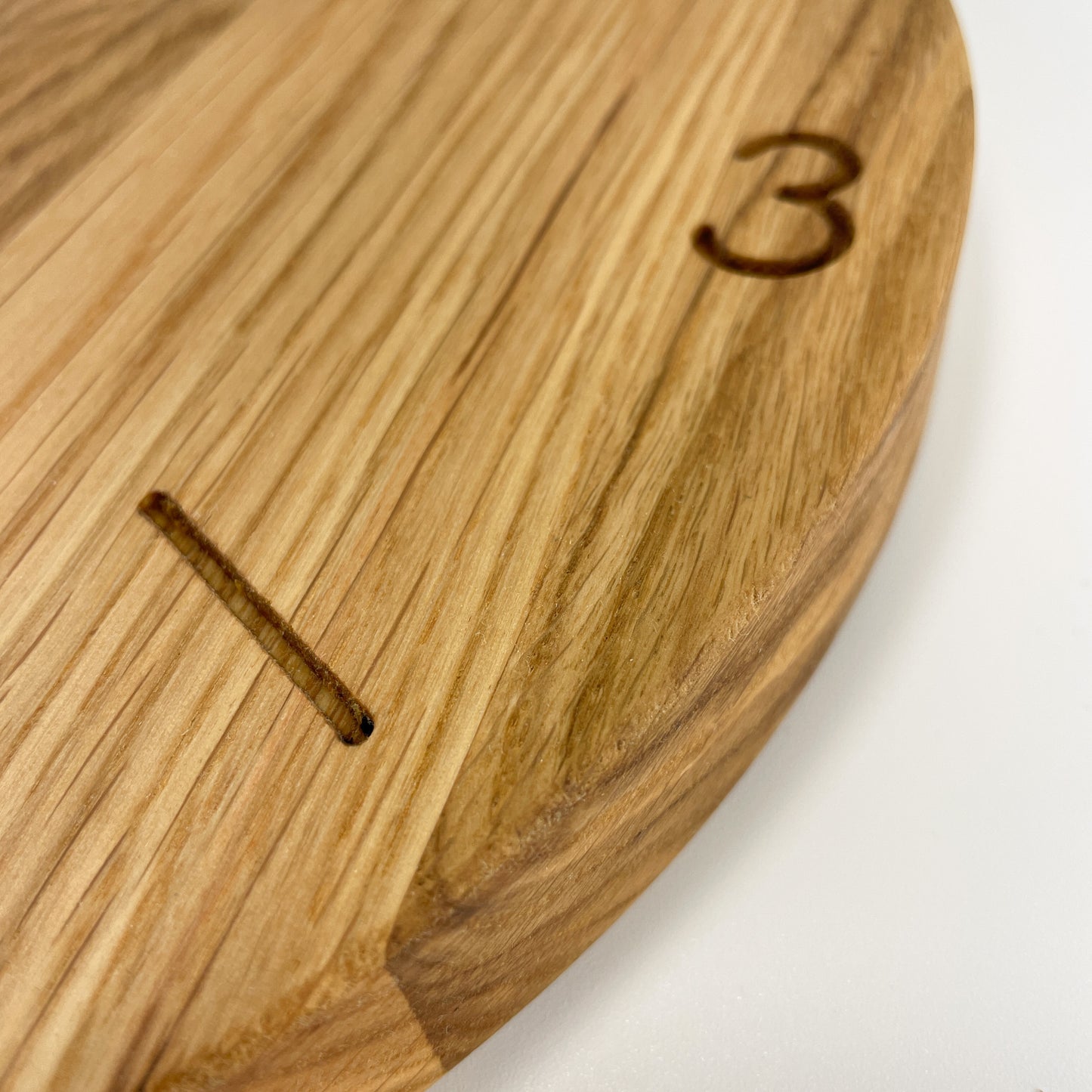 Detailansicht des Rands einer runden Holz-Wanduhr bei der die meisten Stunden durch Striche gekennzeichnet sind.