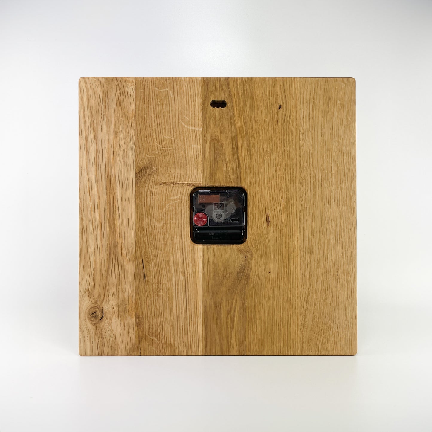 Rückansicht einer eckigen Holz-Wanduhr. Wandaufhängung im oberen Bereich sowie sichtbares Batteriefach und Einstellungsrad für die Zeiger.