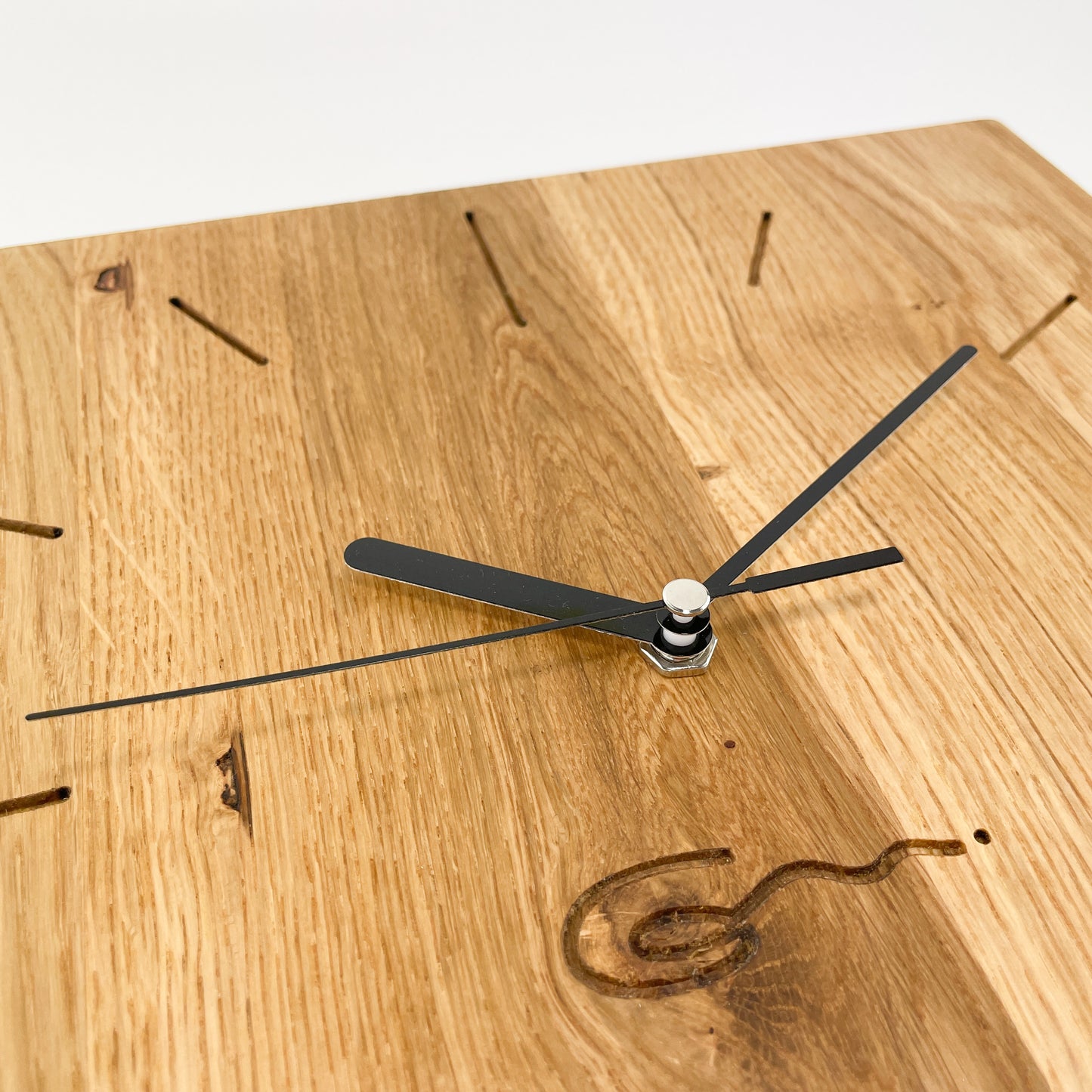 Detailansicht einer eckigen Holz-Wanduhr mit schwarzen Zeigern, bei der die Zahlen die die Stunden durch eingravierte Striche markiert sind