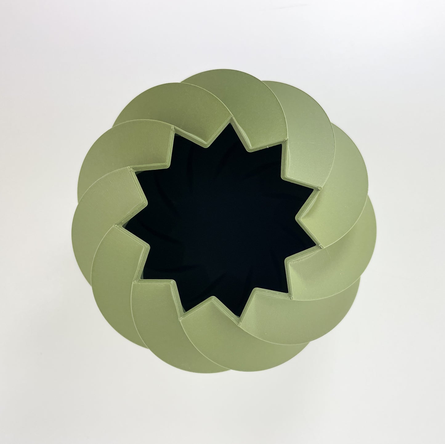 Die rundliche Vase aus moosgrünem Kunststoff mit gedrehter Struktur von oben gesehen. Man sieht das sternförmige Loch mit 11 Zacken und die davon abgehenden Rillen der Vase. Fotografiert wurde sie vor einem weißen Hintergrund.