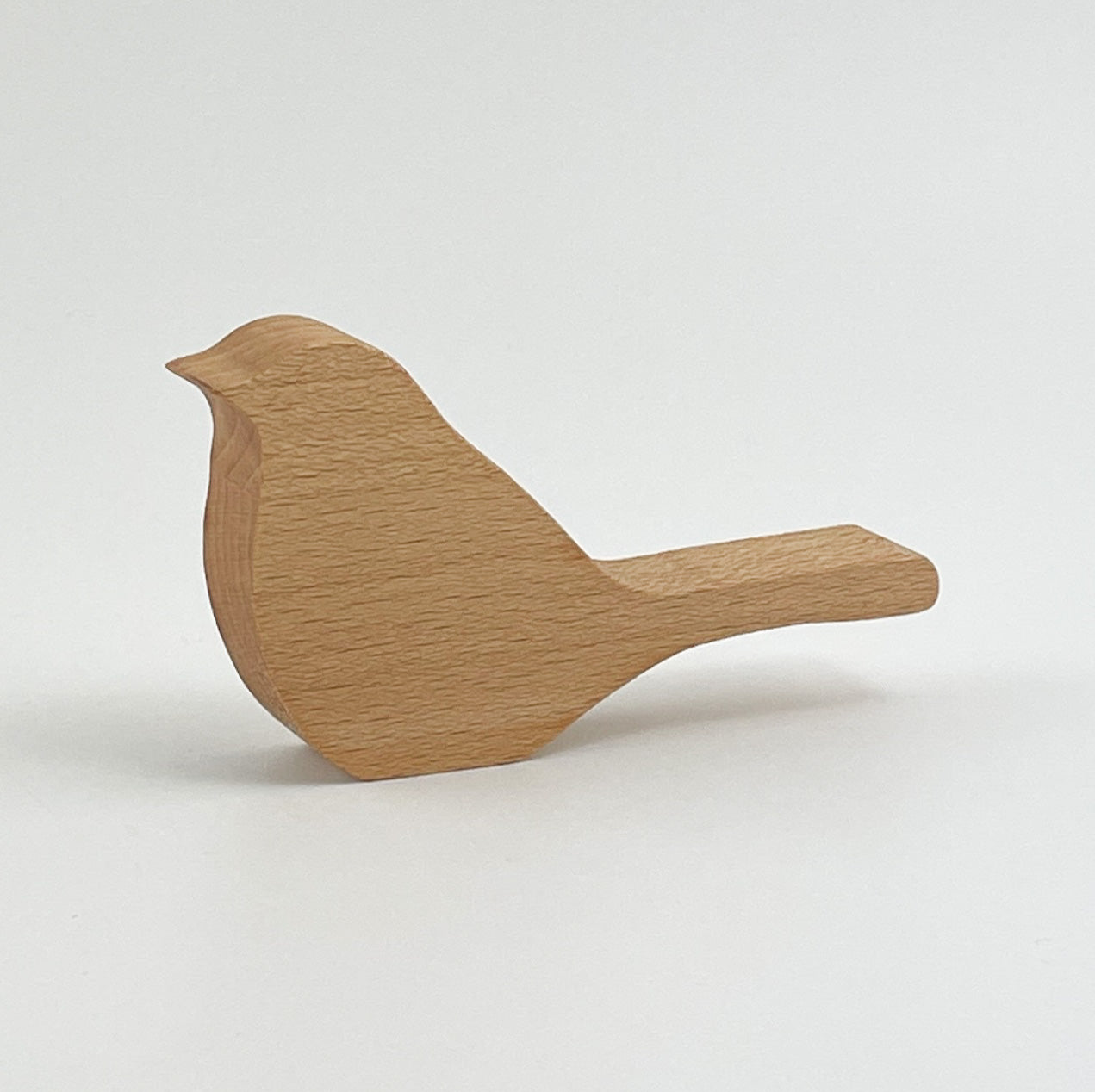 Rückansicht von Holzvogel Kiki, aus Holz gefertigt, präsentiert auf einem neutralen Hintergrund. Das Objekt zeigt eine stilisierte Vogelform, die aus Holz geschnitzt wurde, mit sichtbaren Maserungen und einer glatten Oberfläche, was auf eine hochwertige Verarbeitung hinweist.
