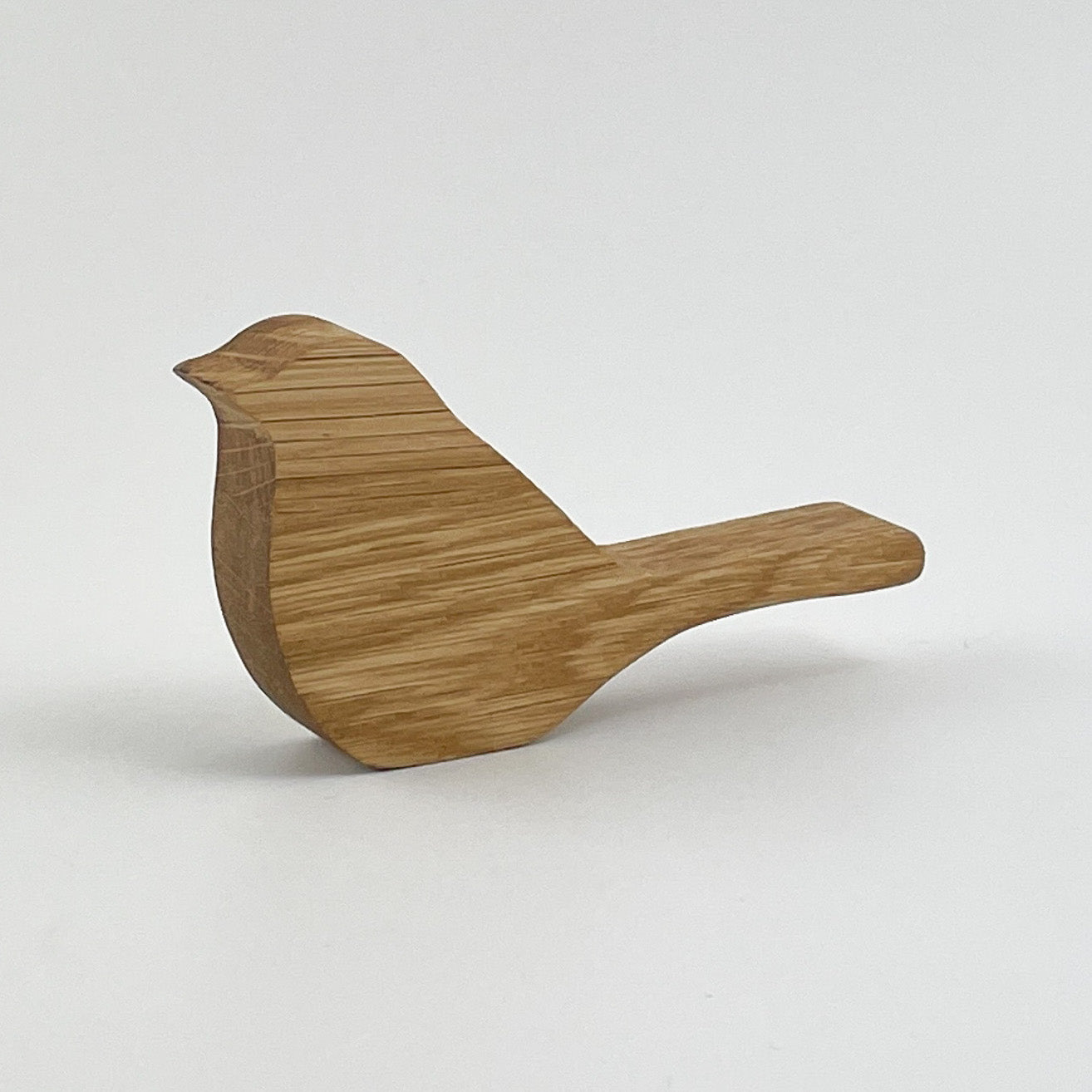 Frontansicht von Holzvogel Kiki, gefertigt, präsentiert auf einem neutralen Hintergrund. Das Objekt zeigt eine stilisierte Vogelform, die aus Holz geschnitzt wurde, mit sichtbaren Maserungen und einer glatten Oberfläche, was auf eine hochwertige Verarbeitung hinweist.