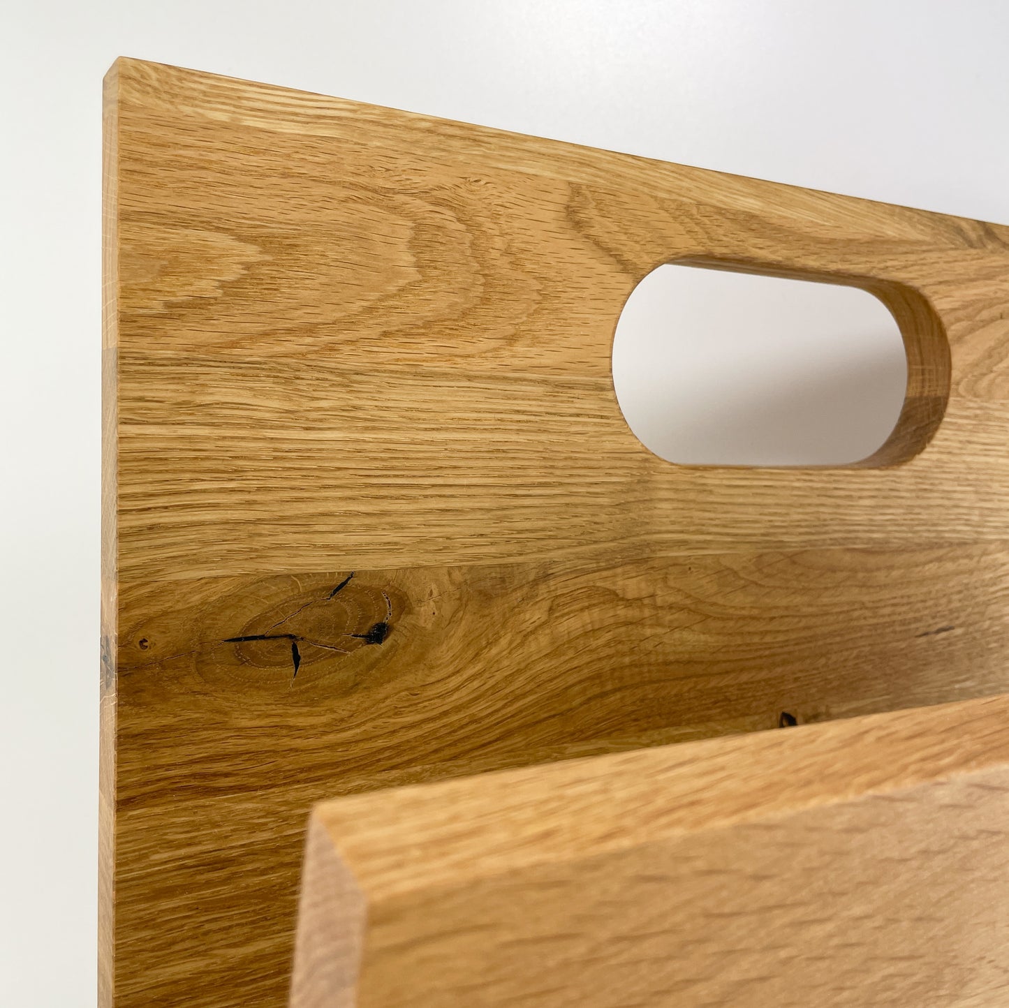 Detailansicht der hinteren, längeren Begrenzung des Stauraum eines Zeitungsständers aus Holz mit Handgriff.