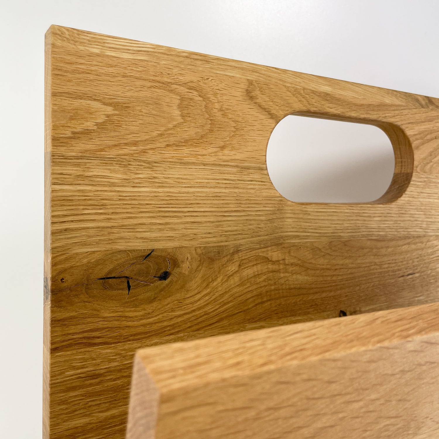 Detailansicht der hinteren, längeren Begrenzung des Stauraum eines Zeitungsständers aus Holz mit Handgriff.