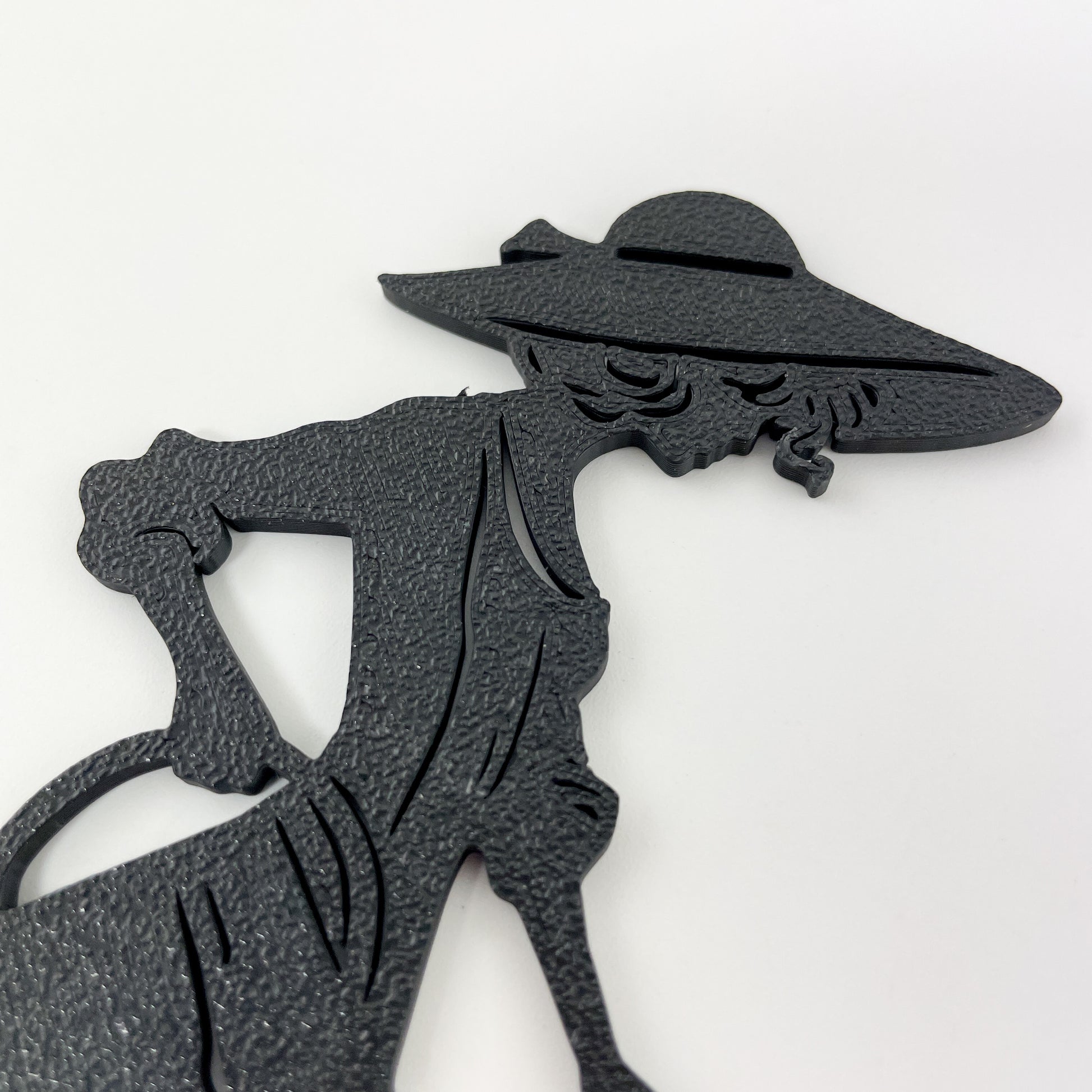 Detailaufnahme der Gärtnerin als Steckbild, die mit dem 3D-Drucker aus schwarzem Kunststoff hergestellt wird. Der Bildbereich zeigt ihren Kopf bis zur Hüfte hinab und die Oberflächenstruktur des Motivs. Der Hintergrund ist Weiß.