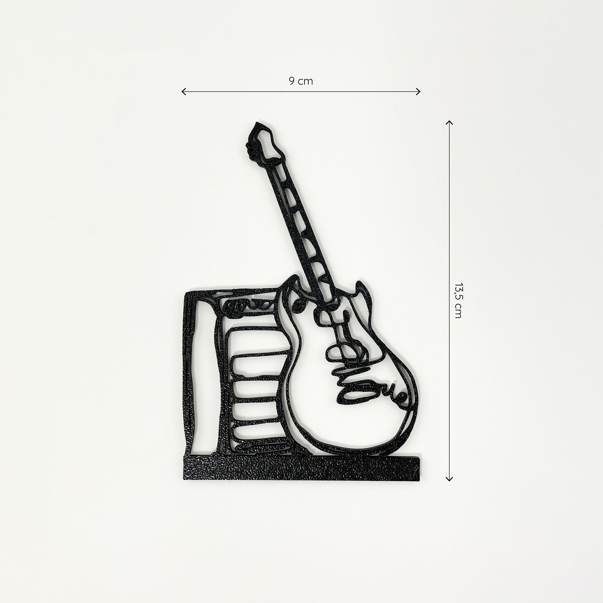 Frontalaufnahme des Steckbildes einer E-Gitarre mit Verstärker im Stil einer Linienzeichnung. Der Hintergrund ist weiß und oberhalb sowie rechts neben dem Motiv sind Maßketten eingezeichnet, welche die Größe definieren - es ist 9cm breit und 13,5cm hoch. Unten befindet sich ein breiterer Streifen, mit dem die E-Gitarre mit Verstärker in einen Halter gesteckt werden kann.