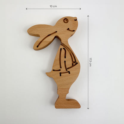 “Paul Buche” - Frontansicht des Osterhasen aus Holz. Der Hase ist stehend dargestellt, mit einer Höhe von 17.5 cm und einer Breite von 10 cm. Er hat eine natürliche Holzfarbe und zeigt Details wie Augen, Nase, Mund und Konturen des Körpers eingebrannt oder eingeritzt.