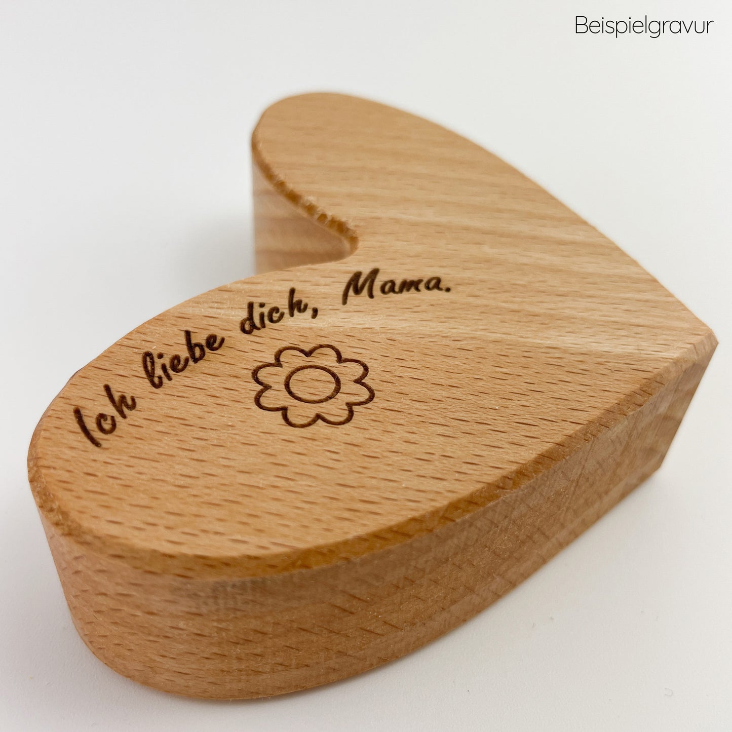 Detailansicht von Holzherz Holli, mit der Gravur “Ich liebe dich, Mama” und einer kleinen Blumenverzierung. Die Holzmaserung ist sichtbar und verleiht dem Herz eine natürliche und warme Ästhetik.