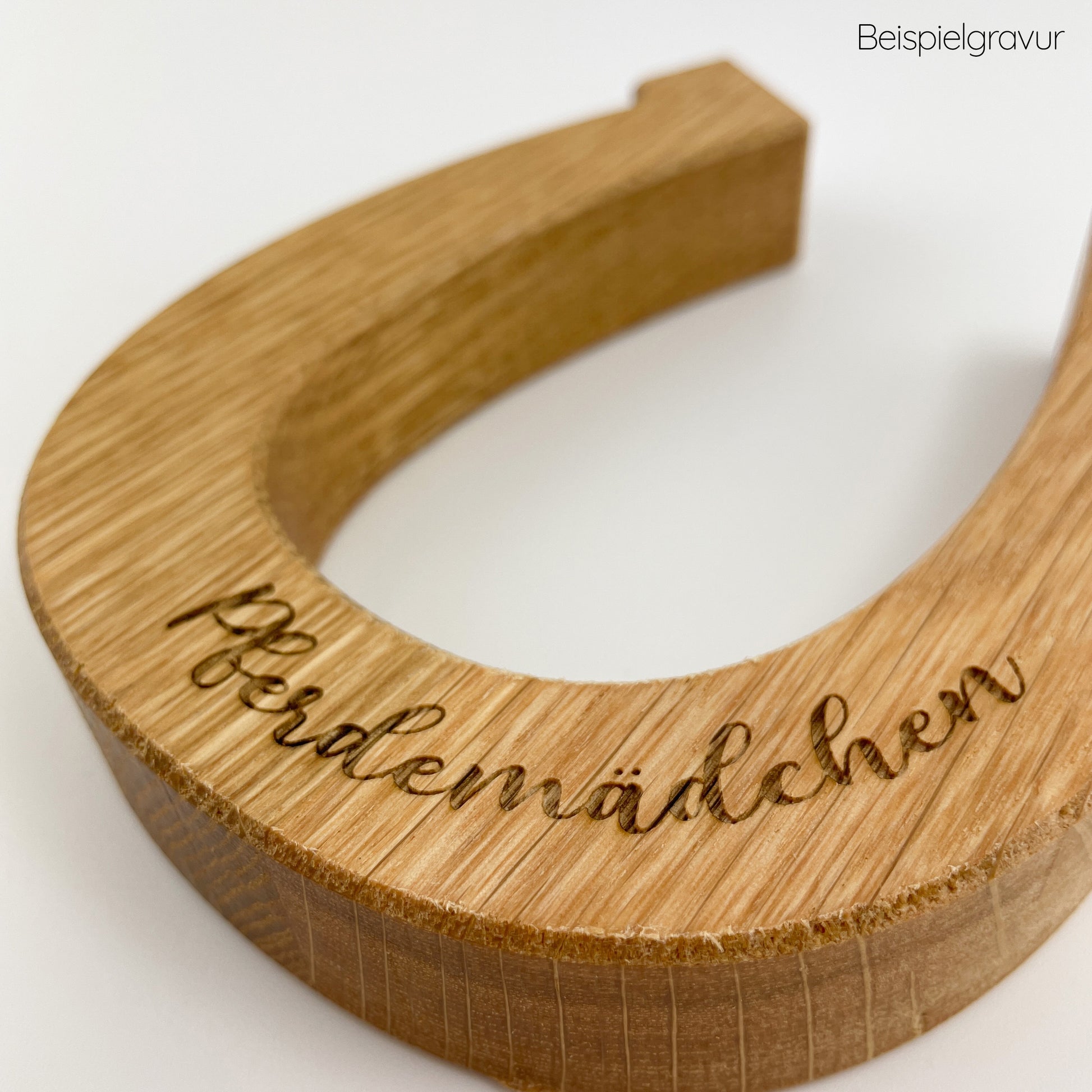 Detailansicht von einesHufeisen aus Holz - Hugo, auf einem weißen Untergrund liegend. In einer geschwungenen Schreibschrift ist das Wort "Pferdemädchen" in Form einer Gravur zu sehen.