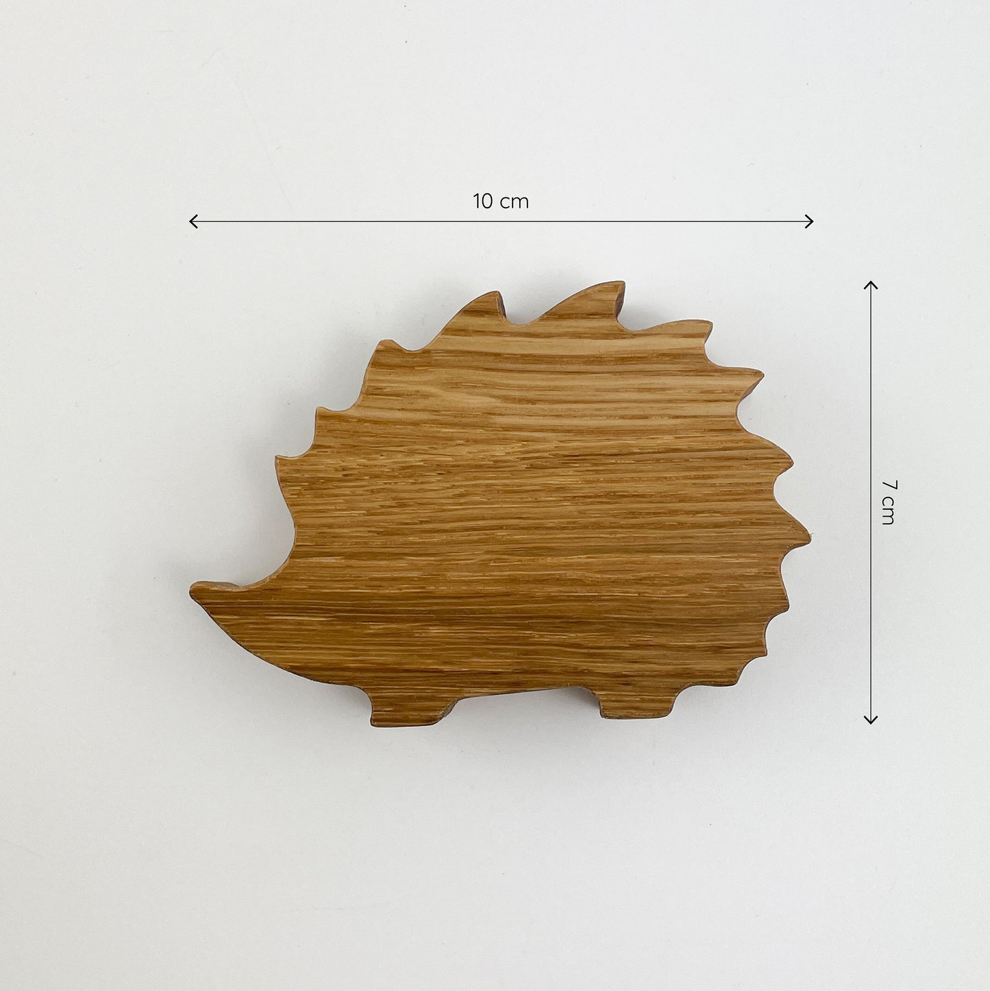 Frontansicht von Holz Igel - Laurenz. Die Maße sind 10 cm und 7 cm. Die Figur zeigt die charakteristische stachelige Silhouette eines Igels und ist aus Holz mit sichtbarer Maserung gefertigt. Ein Teil der Figur ist durch eine braune Fläche verdeckt.