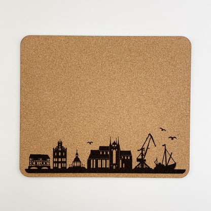 Frontalansicht von ein quadratisches Mousepad aus Kork mit einer dunklen Silhouette einer Stadtskyline und fliegenden Vögeln in der unteren rechten Ecke.