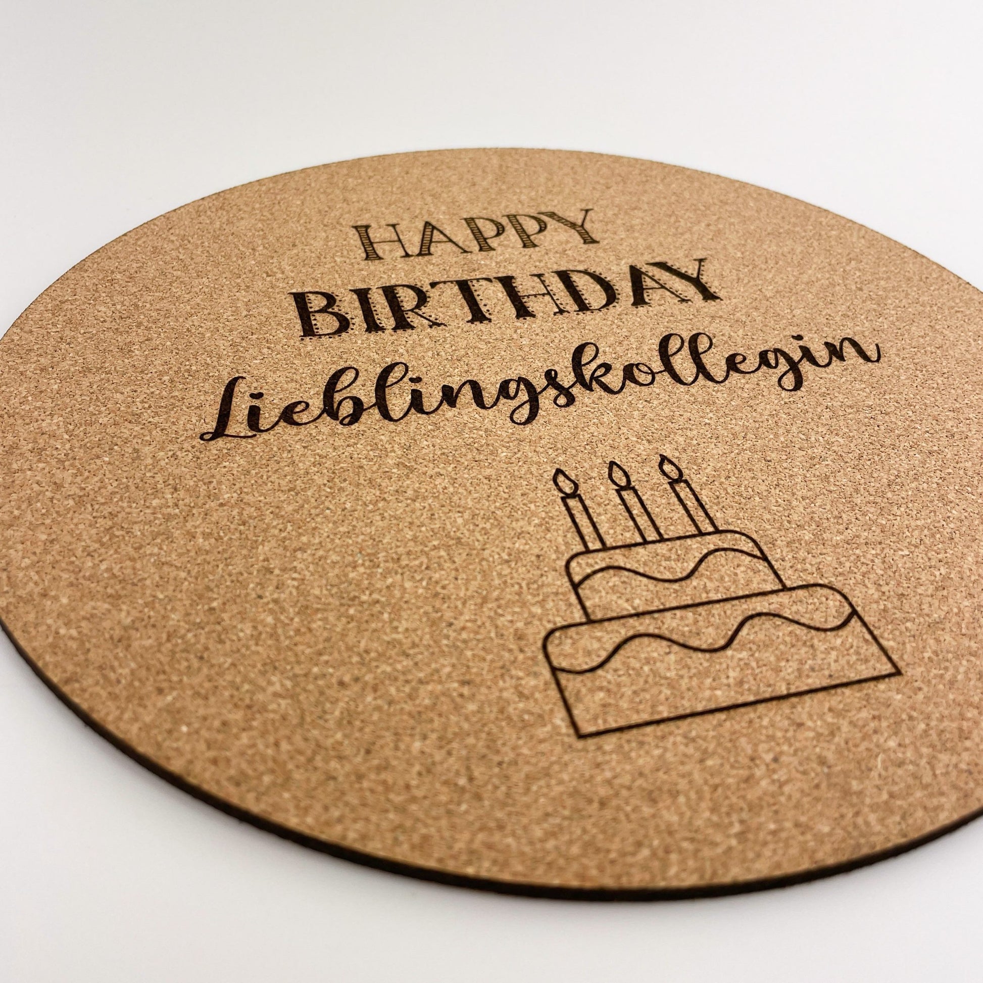 Detailansicht von runde Mousepad aus Kork mit der Aufschrift “HAPPY BIRTHDAY Lieblingskollegin” in schwarzer Schrift. Unter dem Text ist eine einfache Zeichnung eines Geburtstagskuchens mit drei Kerzen abgebildet. Das Design ist schlicht und elegant, was den Mauspad zu einem persönlichen und zugleich praktischen Geschenk macht.