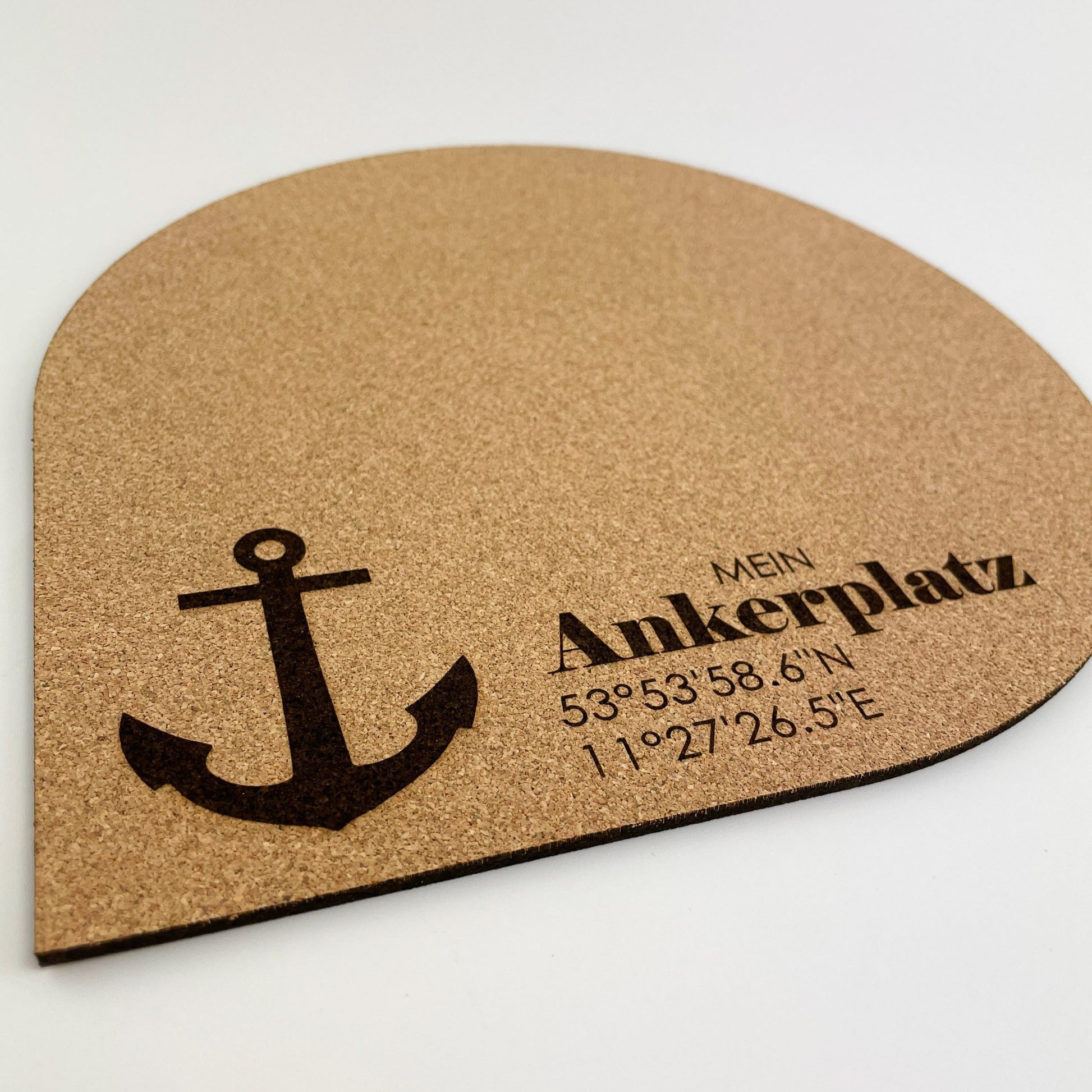 Detailansicht von ein halbrundes Mousepad aus Kork material mit einem aufgedruckten schwarzen Anker in der unteren Mitte. Über dem Anker steht der Text “MEIN ANKERPLATZ” in schwarzer Schrift, darunter sind Koordinaten “53°53’58.6"N 1°02’26.5"E” angegeben.