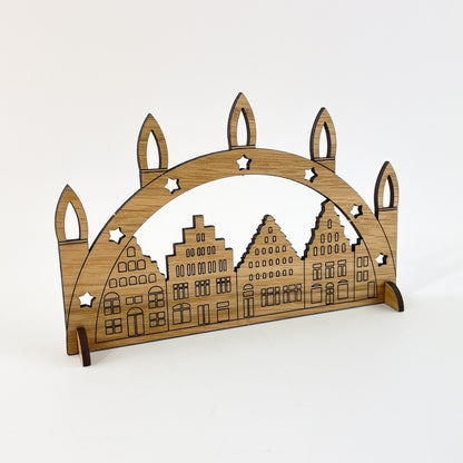 Der aus der Holz-Karte herausgelöste Schwibbogen kann mithilfe der kleinen Standfüße aufgestellt und mehrere Jahre als nachhaltige Weihnachtsdekoration verwendet werden. Das Motiv des Schwibbogens sind die Giebelhäuser der Wismarer Altstadt.