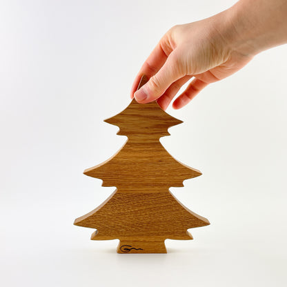 Der minimalistische Deko-Tannenbaum aus Holz wird oben an der Spitze von einer Hand gehalten und steht gerade ausgerichtet vor einem neutralen weißen Hintergrund. Unten im Stamm ist das Firmenlogo der Möbelmanufaktur Goertz eingebrannt.