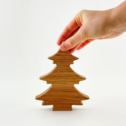 Der kleine Tannenbaum aus Holz vor weißem Hintergrund wird oben an der Spitze von einer Hand gehalten. Er steht gerade zum Betrachter und die Holzmaserung verläuft quer.