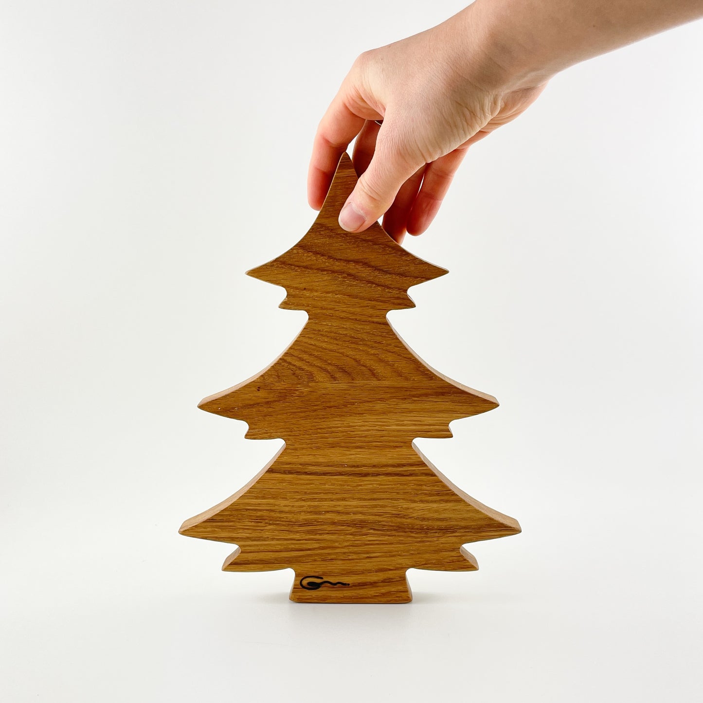 Ein Deko-Tannenbaum aus Holz vor weißem Hintergrund. Eine Hand hält den Baum oben an der Spitze fest und unten im Bereich des Stammes ist das Logo der Goertz Möbelmanufaktur eingebrannt.