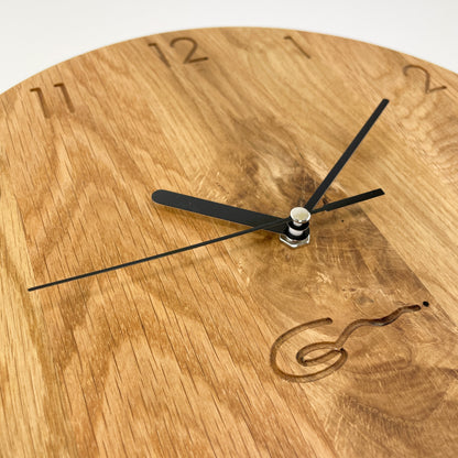 Detailansicht einer runden Holz-Wanduhr mit schwarzen Zeigern, bei der die Zahlen die die Stunden anzeigen eingraviert sind