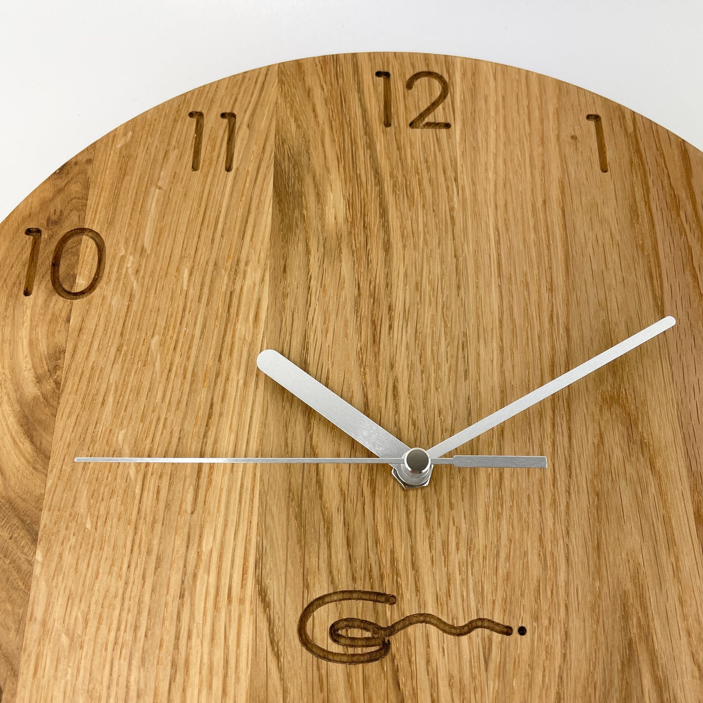 Detailansicht einer runden Holz-Wanduhr mit silbernen Zeigern, bei der die Zahlen die die Stunden anzeigen eingraviert sind