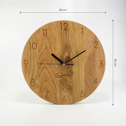 Frontalansicht einer runden Holz-Wanduhr mit schwaruen Zeigern, bei der die Zahlen die die Stunden anzeigen eingraviert sind. Maße von 30x30 cm sind an der rechten und oberen Seite abgebildet.