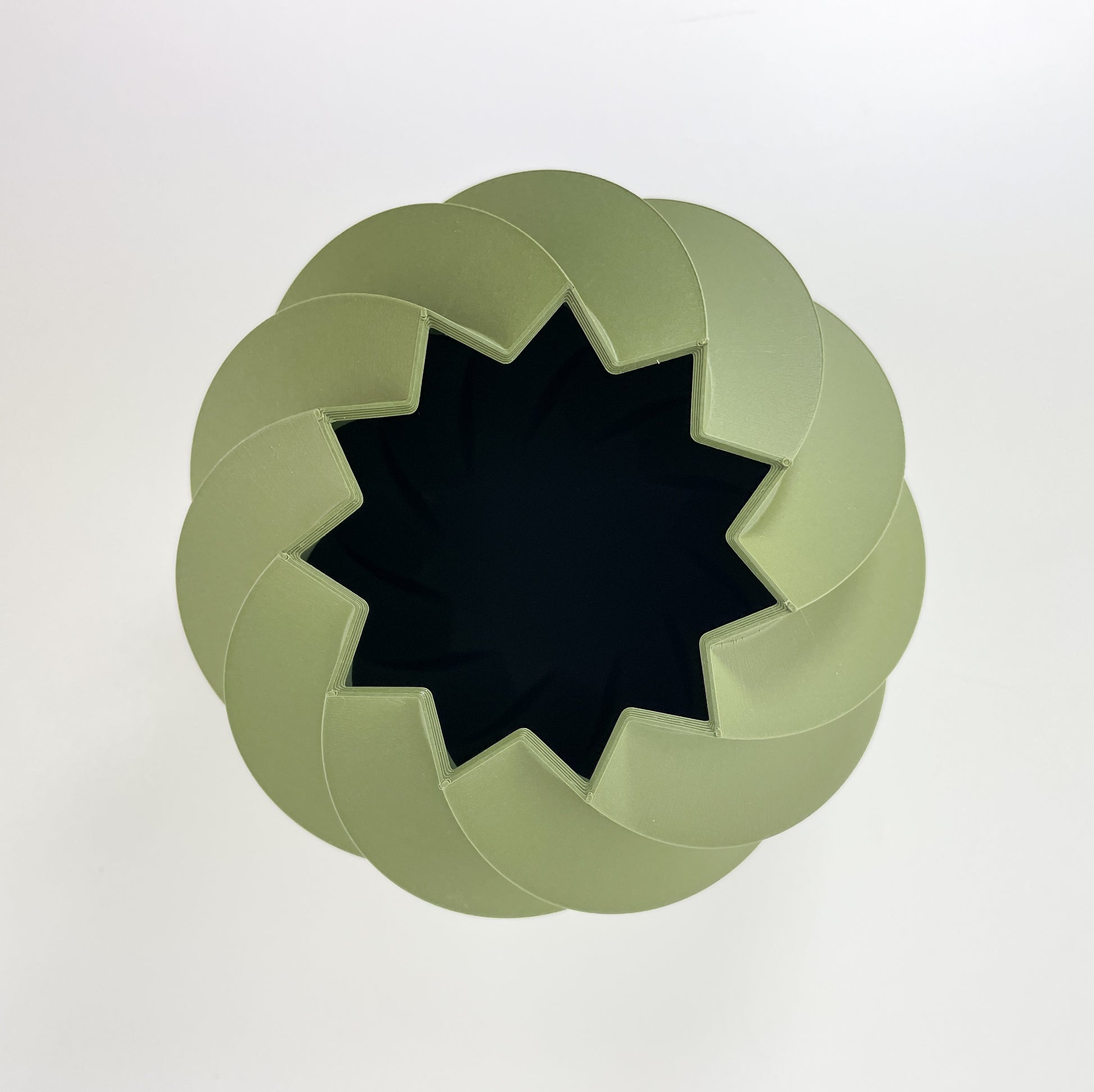 Die rundliche Vase aus moosgrünem Kunststoff mit gedrehter Struktur von oben gesehen. Man sieht das sternförmige Loch mit 11 Zacken und die davon abgehenden Rillen der Vase. Fotografiert wurde sie vor einem weißen Hintergrund.